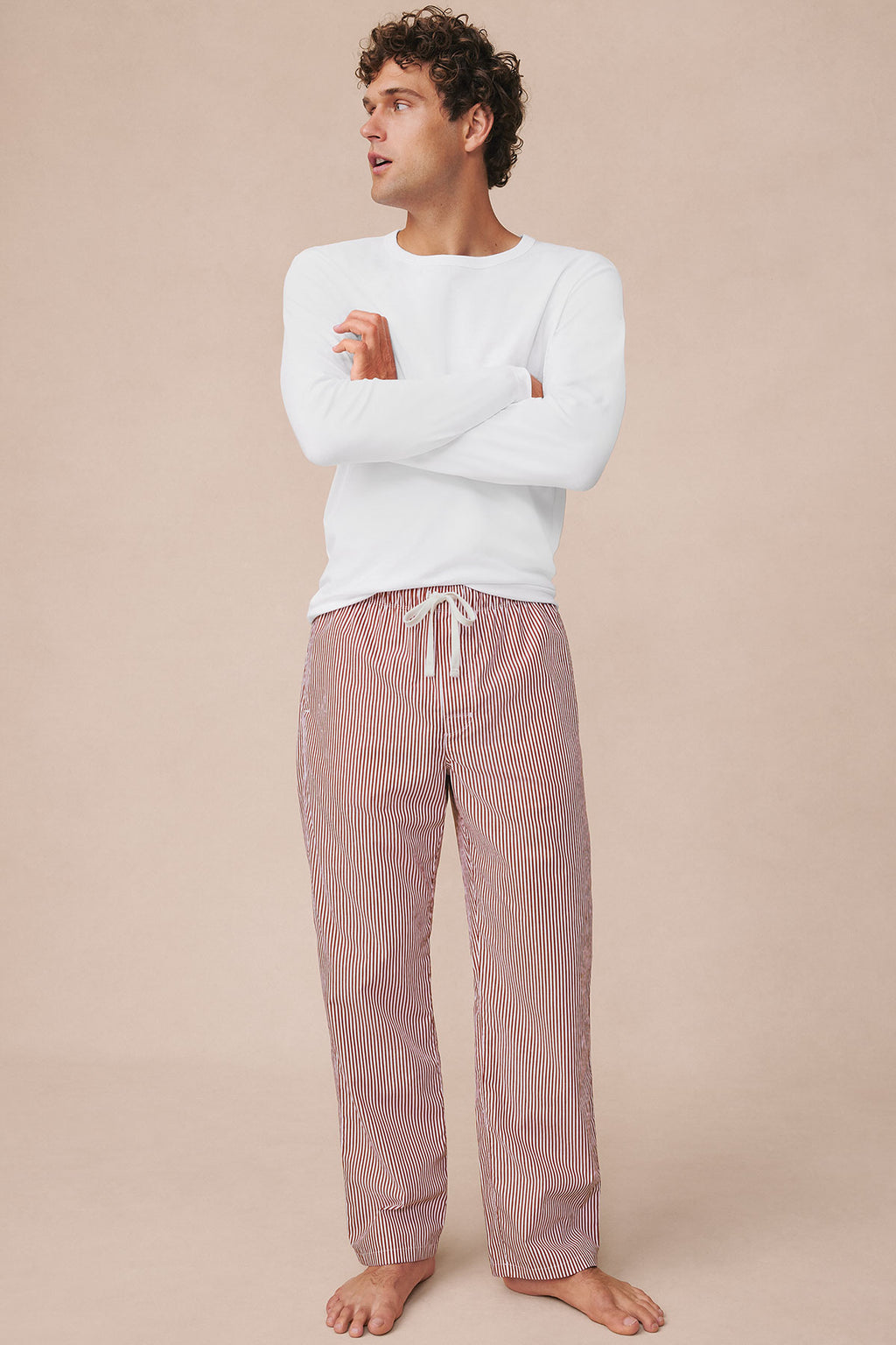 Man wearing white long-sleeve shirt and red and white striped poplin sleep pants with drawstring waist.
