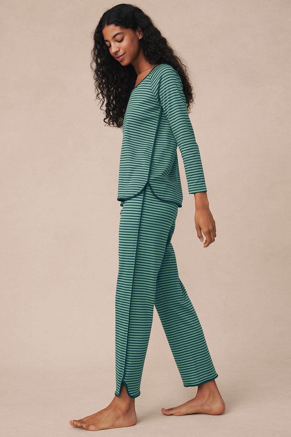 Woman wearing long-sleeve striped pajama set in dark sea green and light green horizontal stripes.
