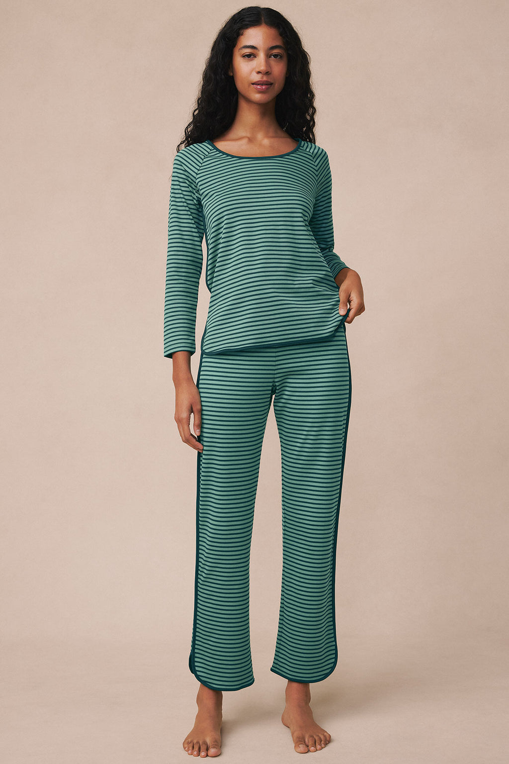 Woman wearing long-sleeve striped pajama set in dark teal and light green horizontal stripes.