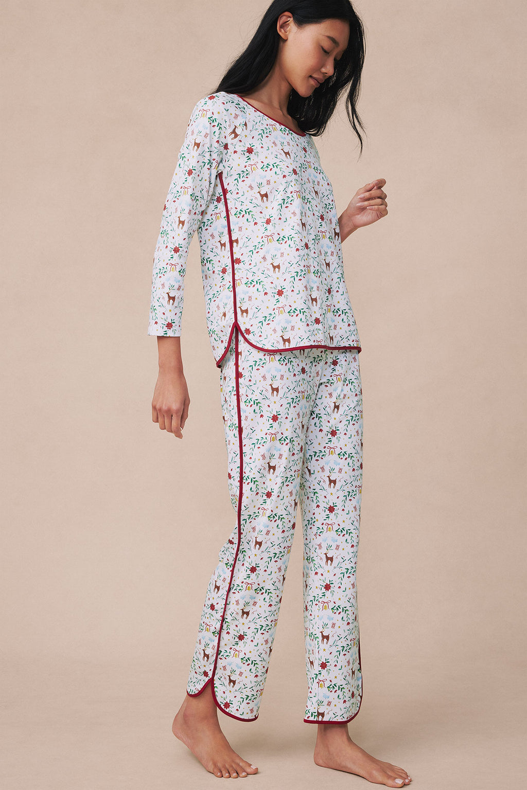 Woman wearing a two-piece pajama set with festive print, three-quarter sleeve top and matching cropped pants with burgundy pi