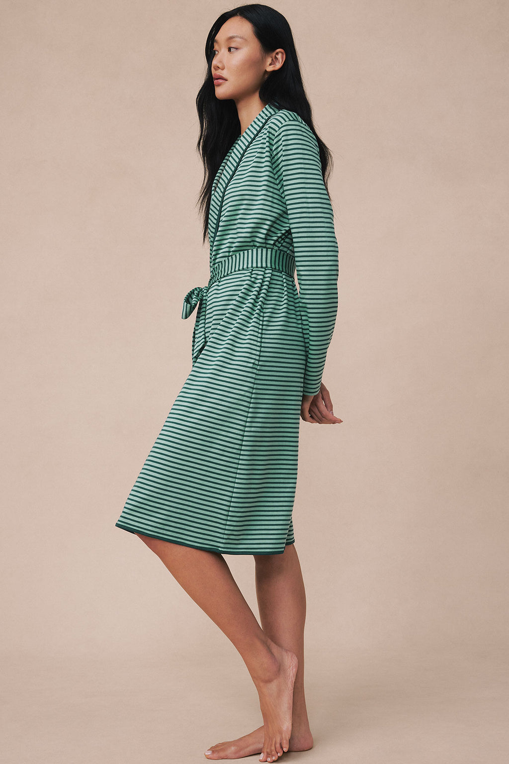 Woman wearing a dark sea and light green striped robe with a tie waist, shown from the side.