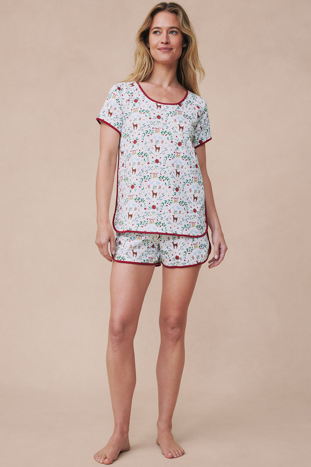 Woman wearing light blue short-sleeve pajama top and shorts with red holiday print and burgundy trim.