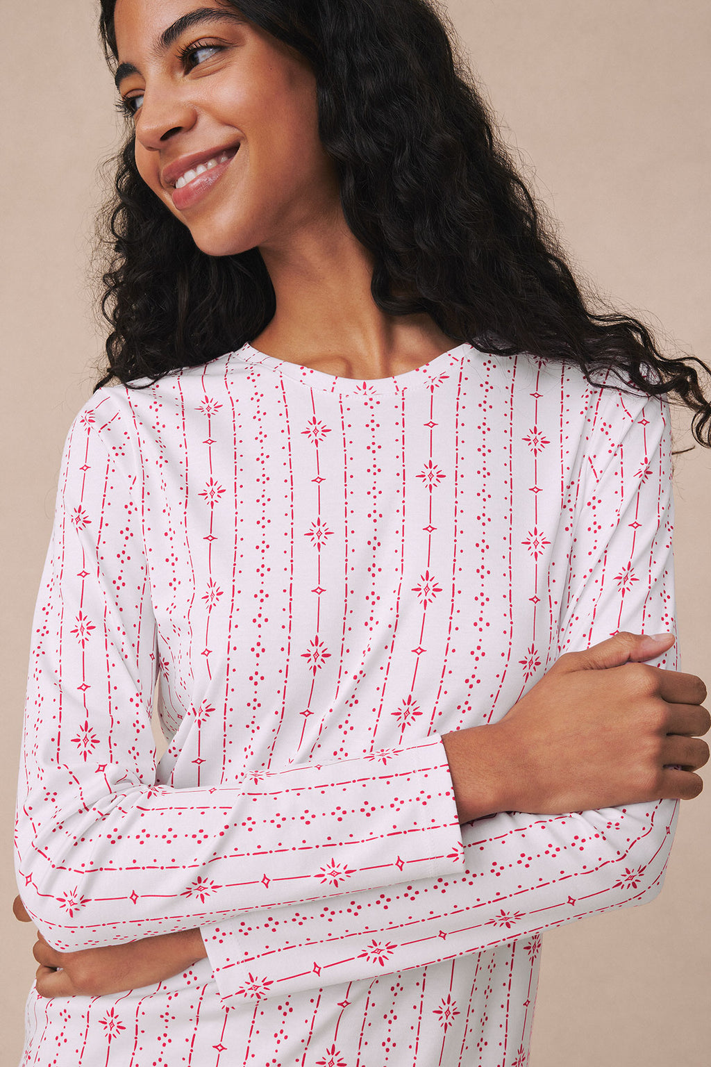 Woman wearing long-sleeved crew neck pajama top with red and white geometric snowflake stripe pattern.