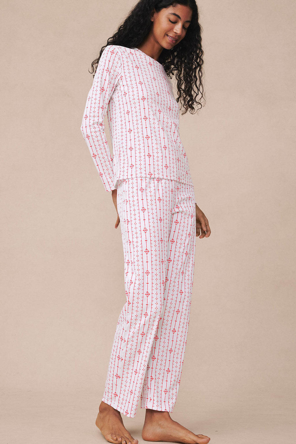 Woman wearing white long-sleeve pajama top and matching full-length pants with red stripe and geometric pattern.