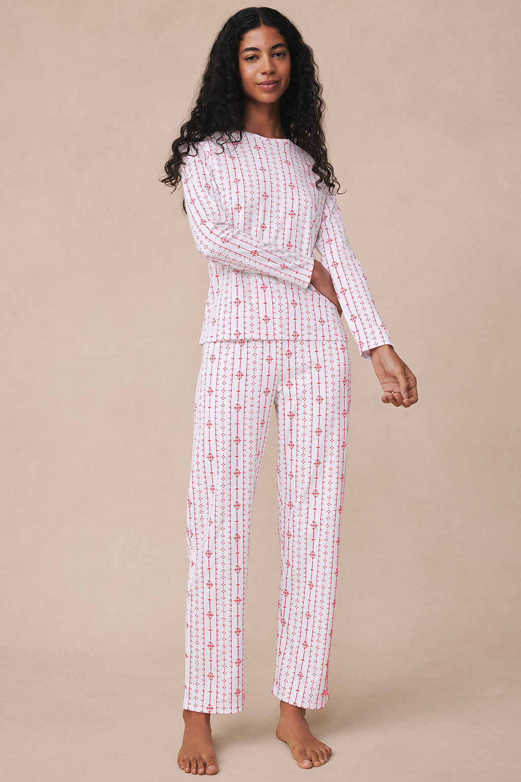 Woman wearing long-sleeved white pajama set with red vertical stripes and geometric pattern throughout.