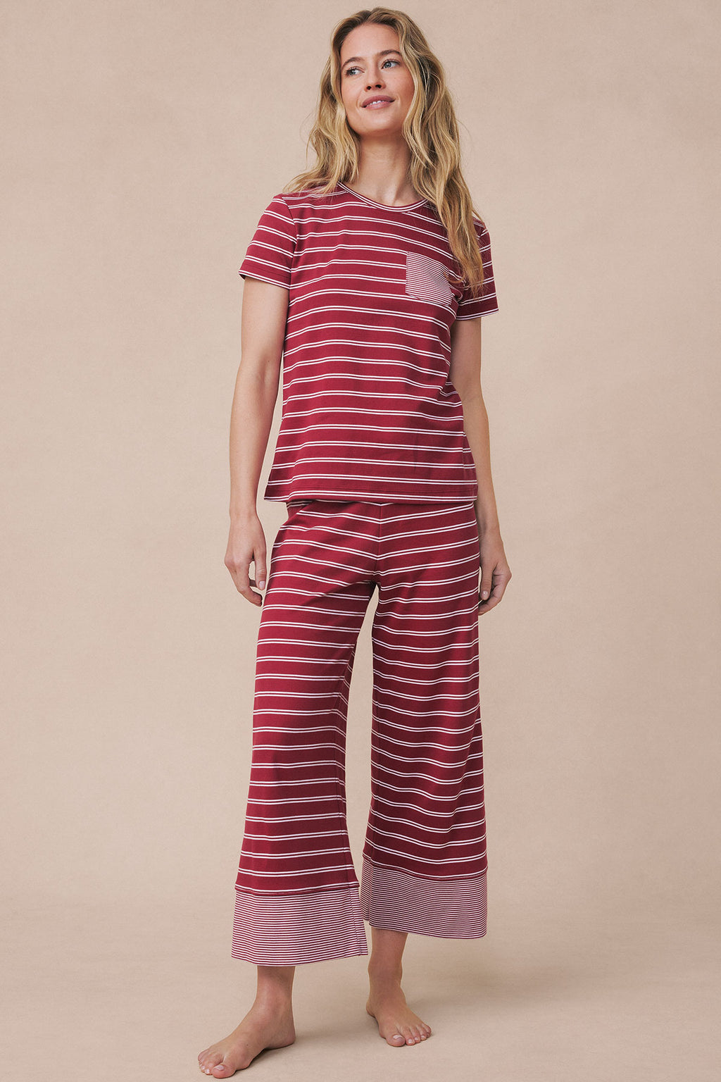Woman wearing garnet and white striped short-sleeve pajama top with matching wide-leg cropped pants featuring striped cuffs.