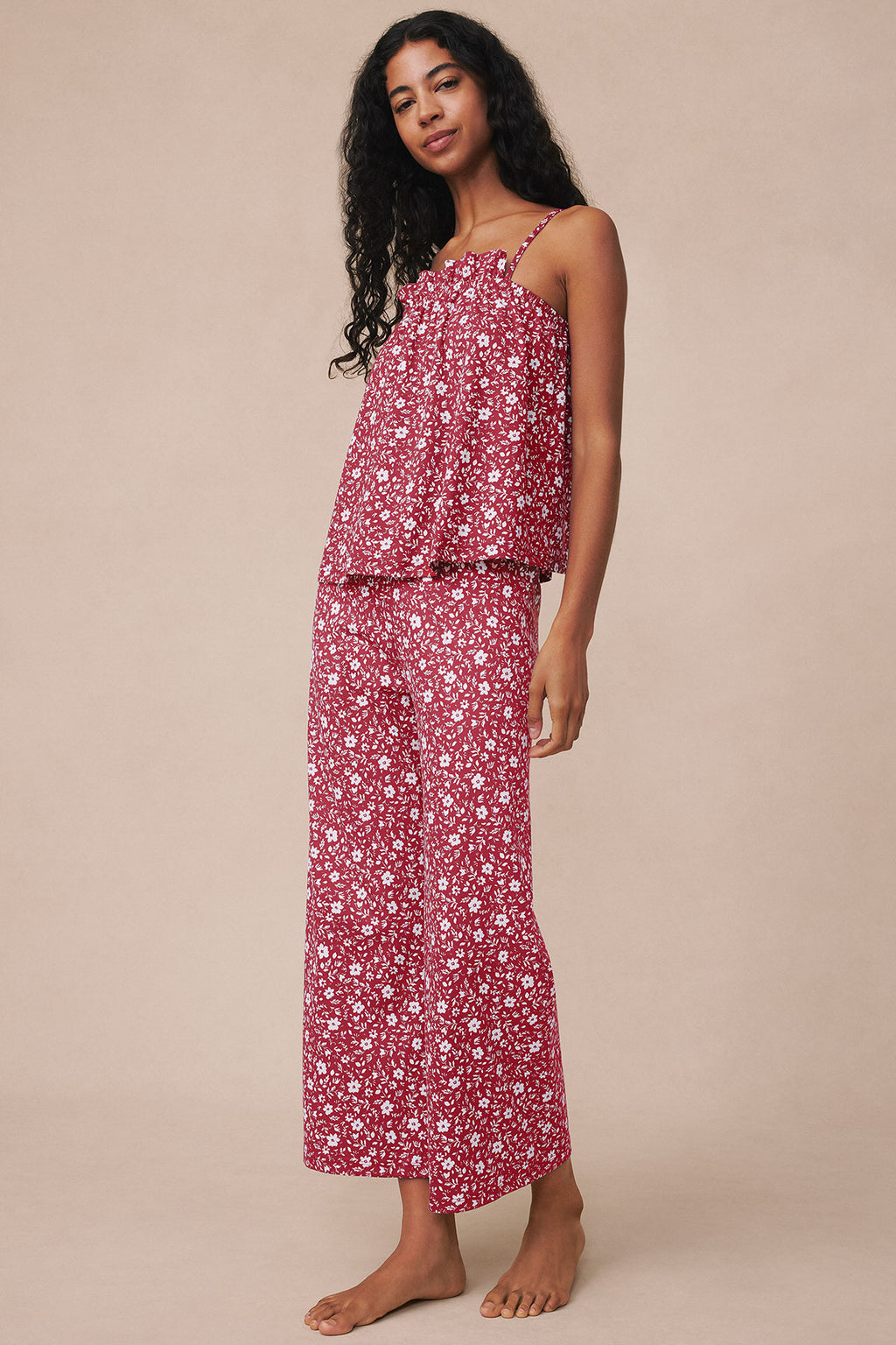 Woman wearing garnet floral two-piece pajama set with ruffled camisole top and matching pants.