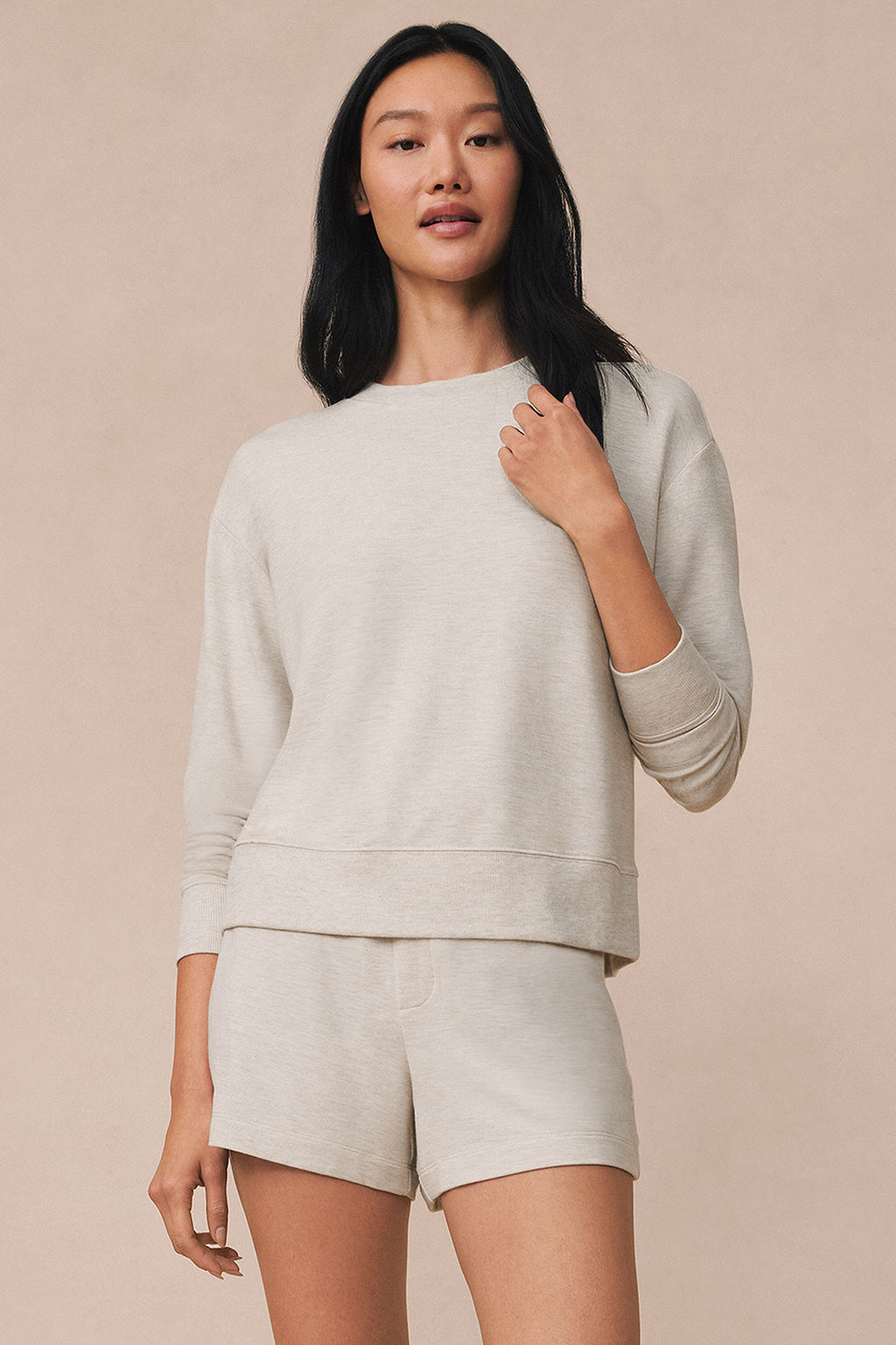 Woman wearing oat heather crewneck sweatshirt and shorts against neutral background.