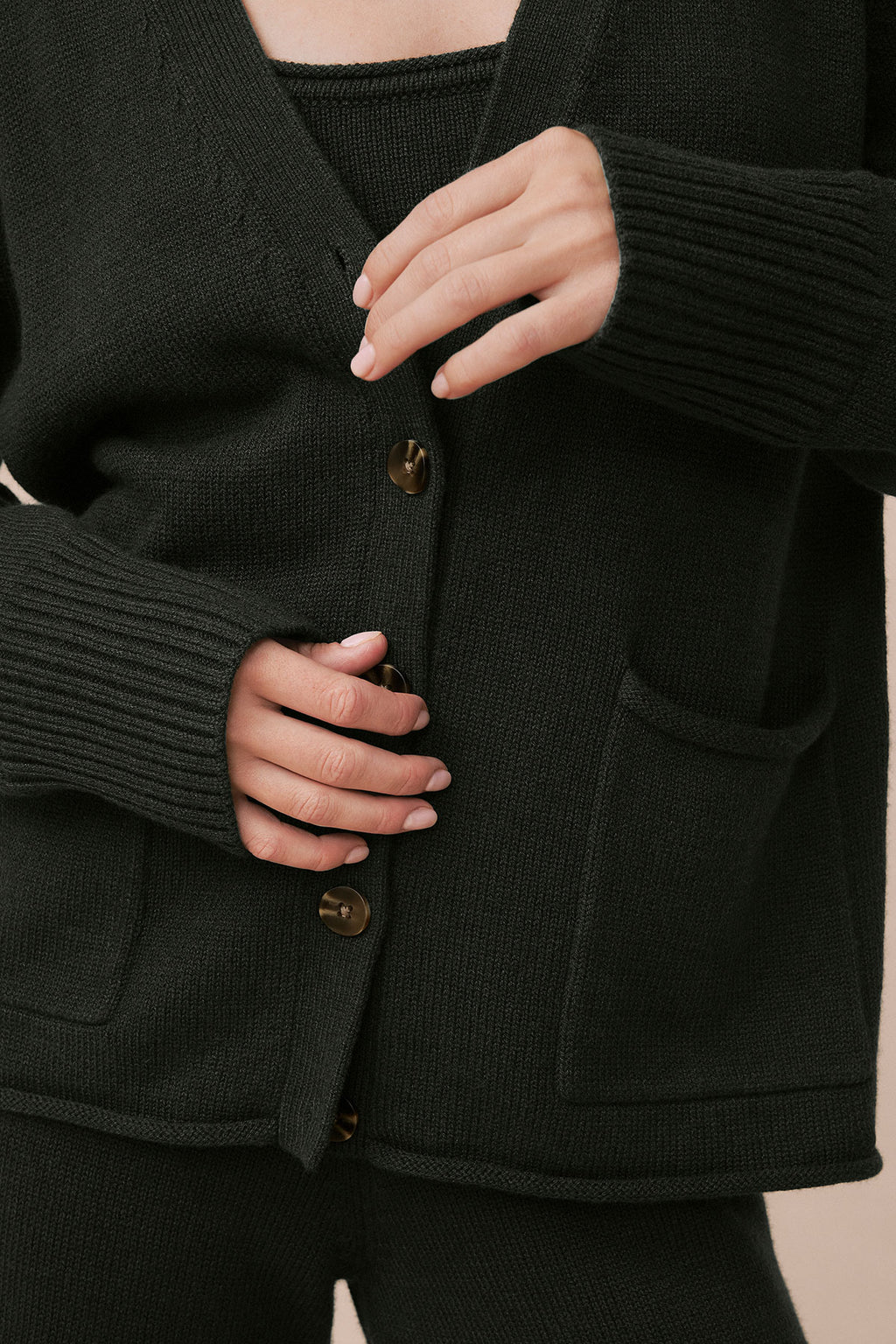 Dark green knit cardigan with ribbed trim and gold button closures, worn over matching ribbed knit top.