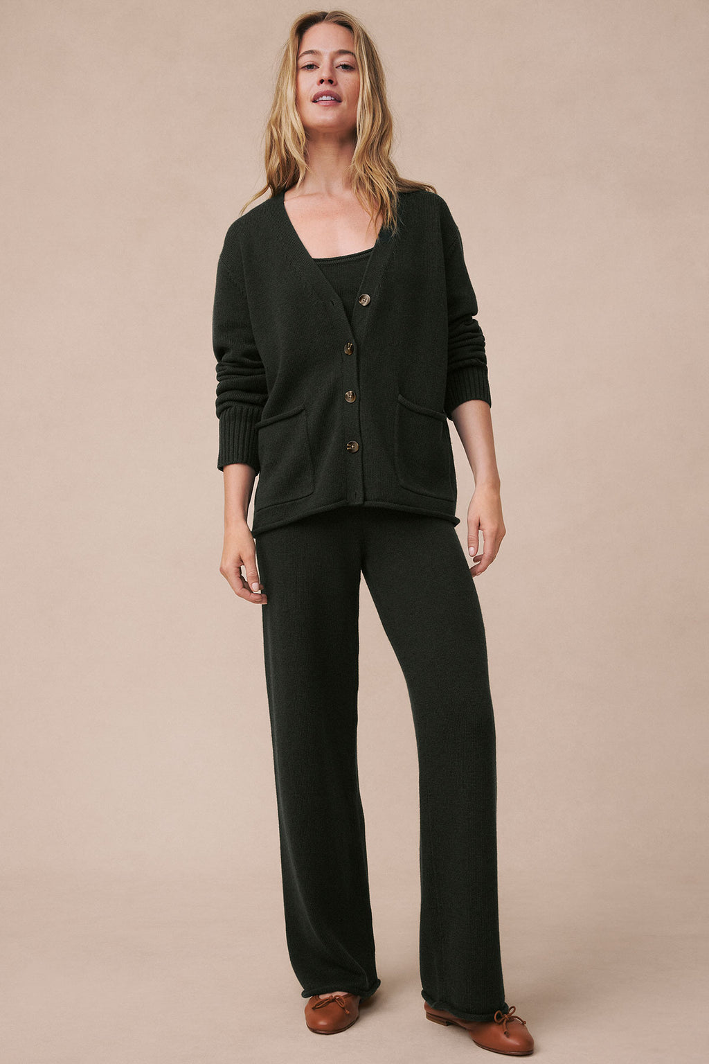 Woman wearing a dark green button-front cardigan and matching wide-leg pants with brown slip-on shoes.