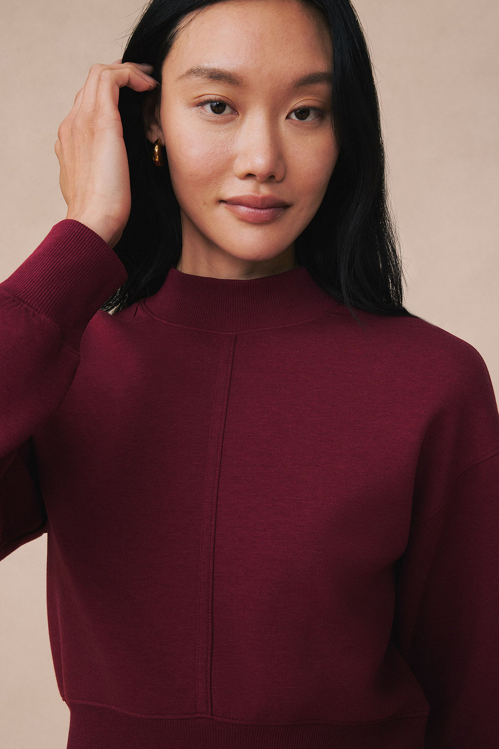 Person wearing burgundy ribbed long-sleeve sweater with crew neckline against neutral background.