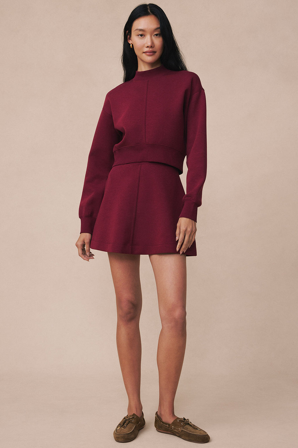 Burgundy two-piece set with long-sleeve crop top and high-waisted mini skirt, styled with brown boat shoes.