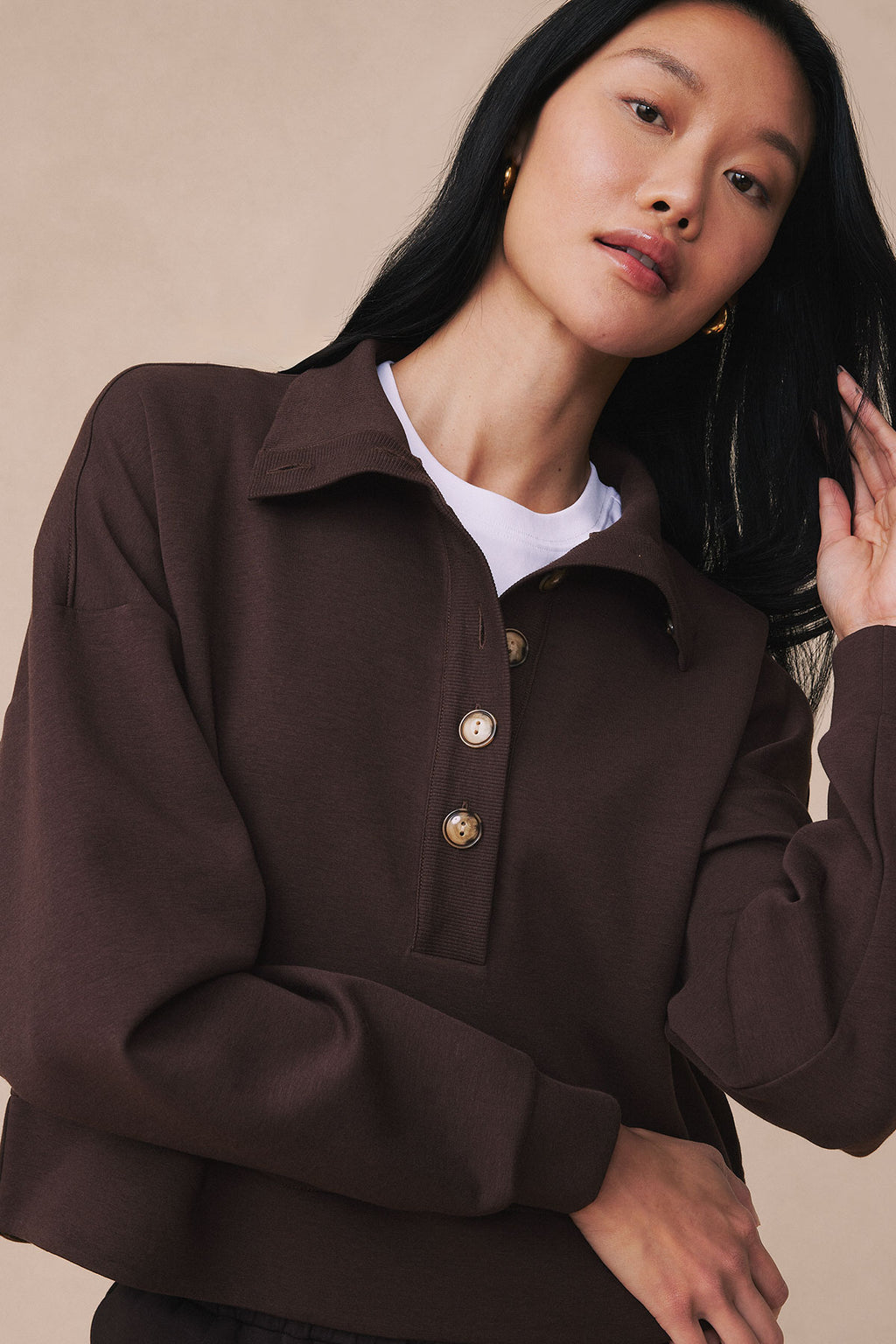 Dark brown pullover with white undershirt, button front, and ribbed texture on model against neutral background.