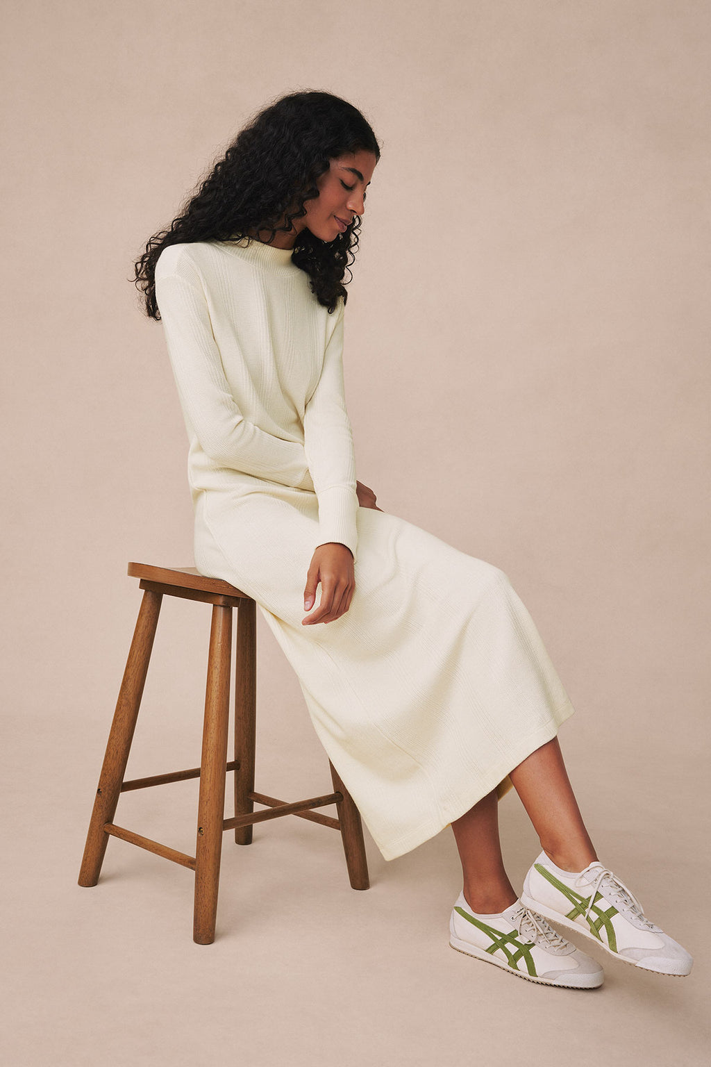 Ivory waffle knit midi dress with long sleeves, shown on model seated on wooden stool.