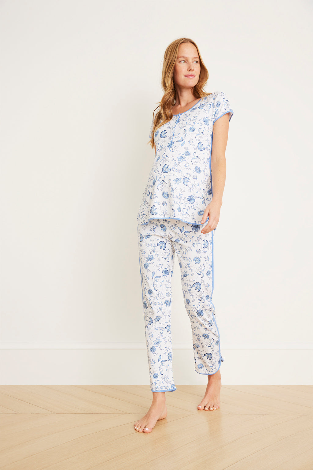 Woman wearing white maternity pajama set with blue floral vine print, short-sleeve top and full-length pants.