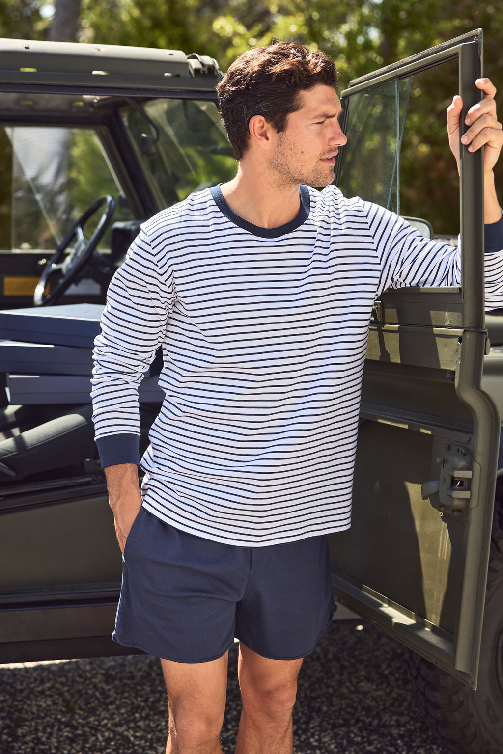 A man in a Mens Pima Long-Short Set in Eclipse stands beside the open door of a green off-road vehicle, looking to the side as sunlight filters through trees in the background.