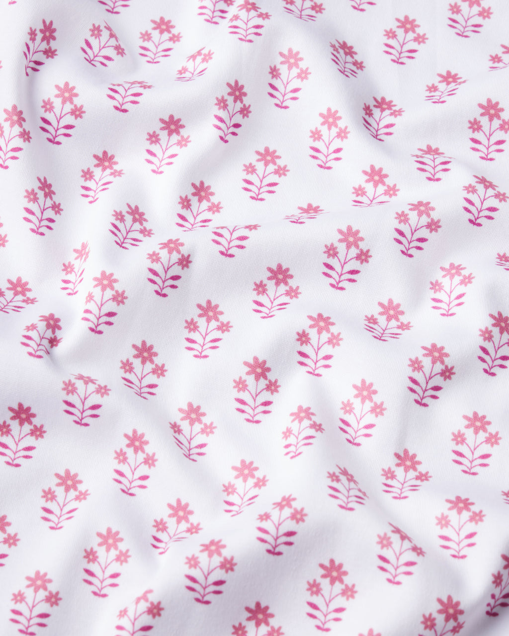 The Pima Long-Long Set in Light Camellia Posy features white Pima cotton fabric adorned with a repeating pattern of small pink flowers and leaves, adding delicate shadows and soft texture to the surface.