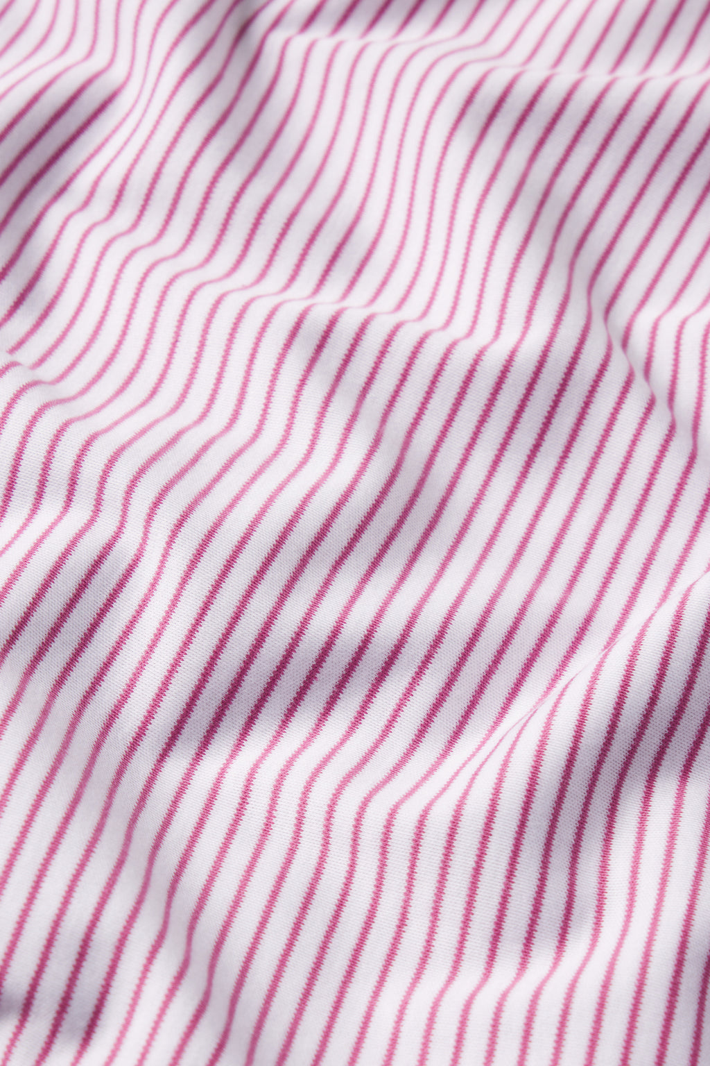 Close-up of the Pima Maternity Wide Leg Pajama Set in Camellia Stripe shows soft white fabric with evenly spaced, wavy pink stripes. Gentle folds and shadows highlight the texture and flowing movement of this cozy maternity pajama set.
