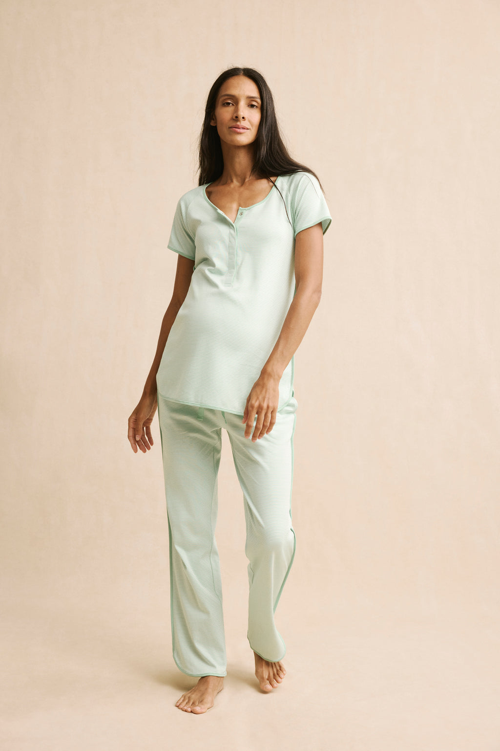 A woman models the Pima Maternity Short-Long Set in Parisian Green, featuring soft Pima cotton with a buttoned short-sleeve top and relaxed-fit pants, posing against a plain beige background to showcase this cozy pajama set.