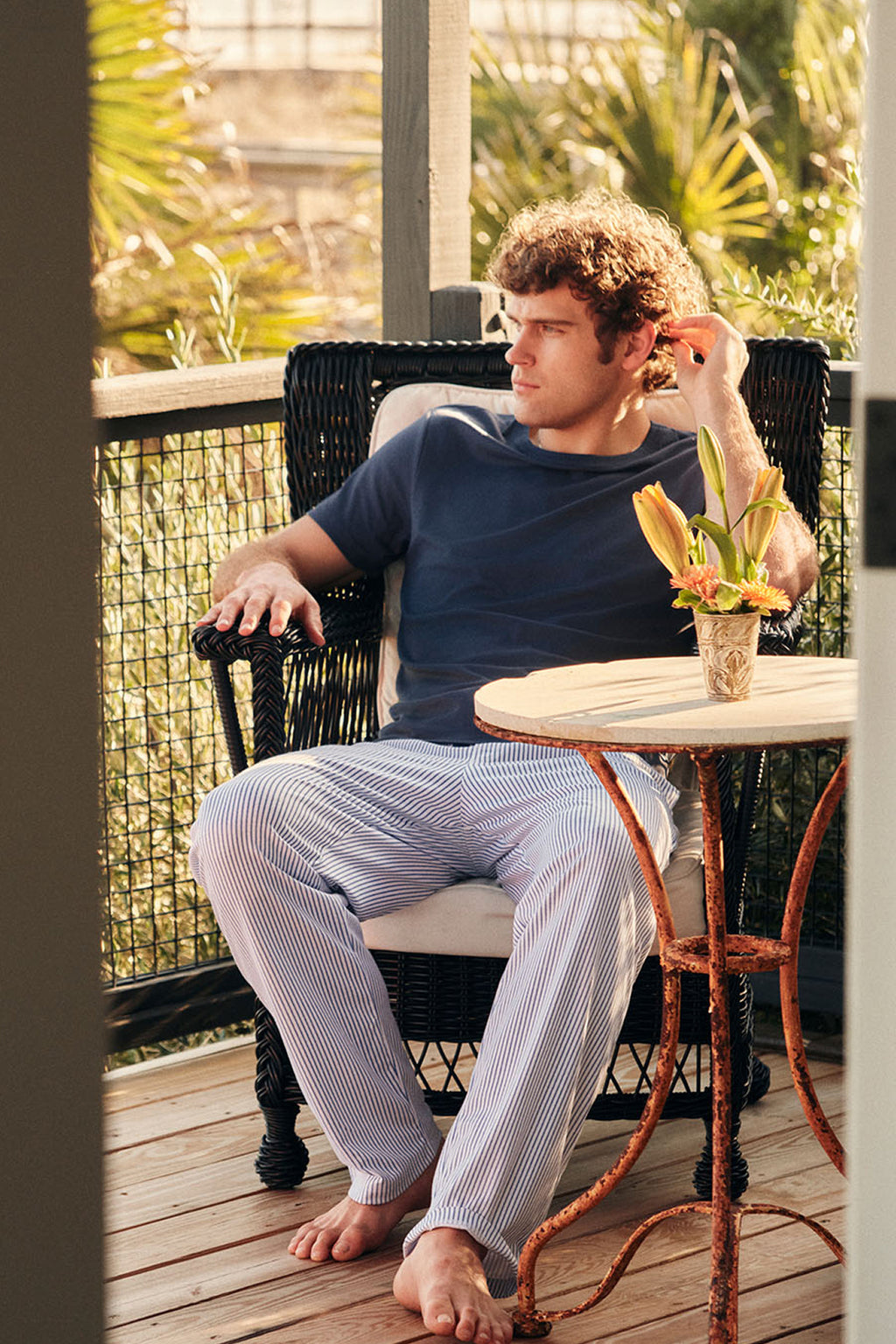 Man wearing navy short-sleeve top and striped long sleep pants sitting outdoors.
