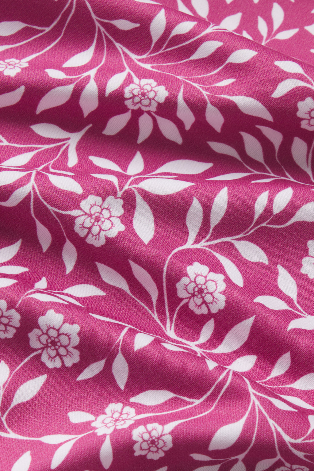 The Pima Long Sleeve Nightgown in Camellia Cecil Floral features pink fabric with a white floral and leafy vine pattern. The cotton material has subtle wrinkles, creating soft folds and shadows on the surface.