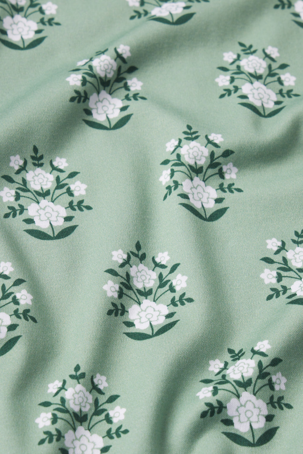 A close-up of soft, green fabric with white flower and leaf patterns featuring gentle folds—perfect for the Pima Crew Wide Leg Pajama Set in Granite Green Cottage Floral.