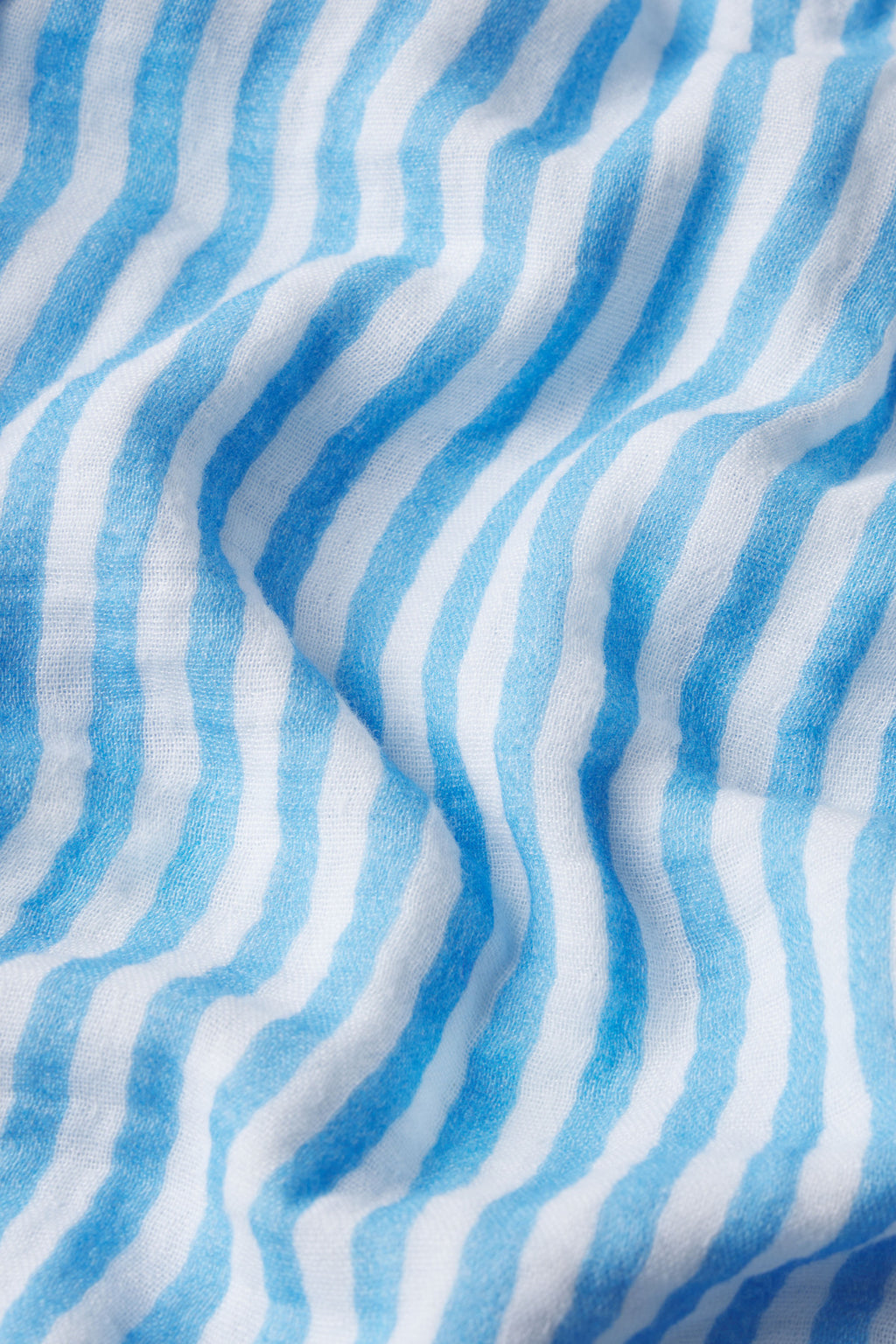 Close-up of gauze fabric with wavy light and dark blue stripes on white, highlighting the soft texture and gentle folds of the Hamptons Pants Set in Sail Blue Awning Stripe—ideal for hot sleepers.