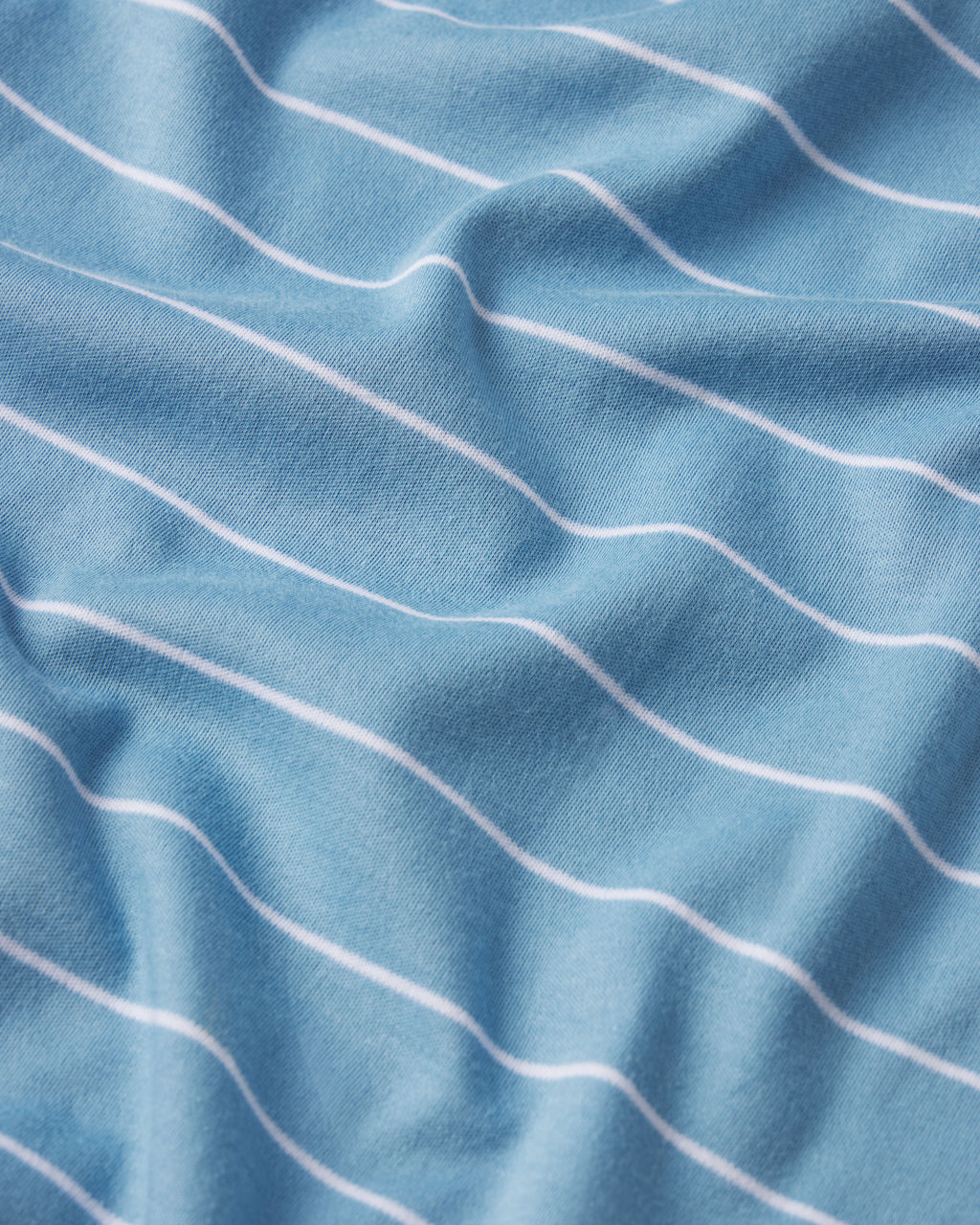 A close-up of the Pima Ruffle Pants Set in Serene Blue Boating Stripe, showcasing soft light blue Pima cotton fabric with thin, evenly spaced horizontal white stripes and gentle folds.