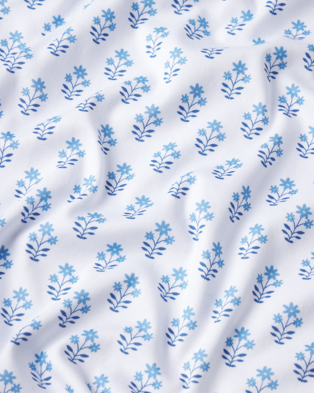 The Pima Shorts Set in Serene Blue Posy features white fabric with a delicate blue floral pattern. Soft creases and luxe Pima cotton make it the ideal choice for cozy, comfortable loungewear.