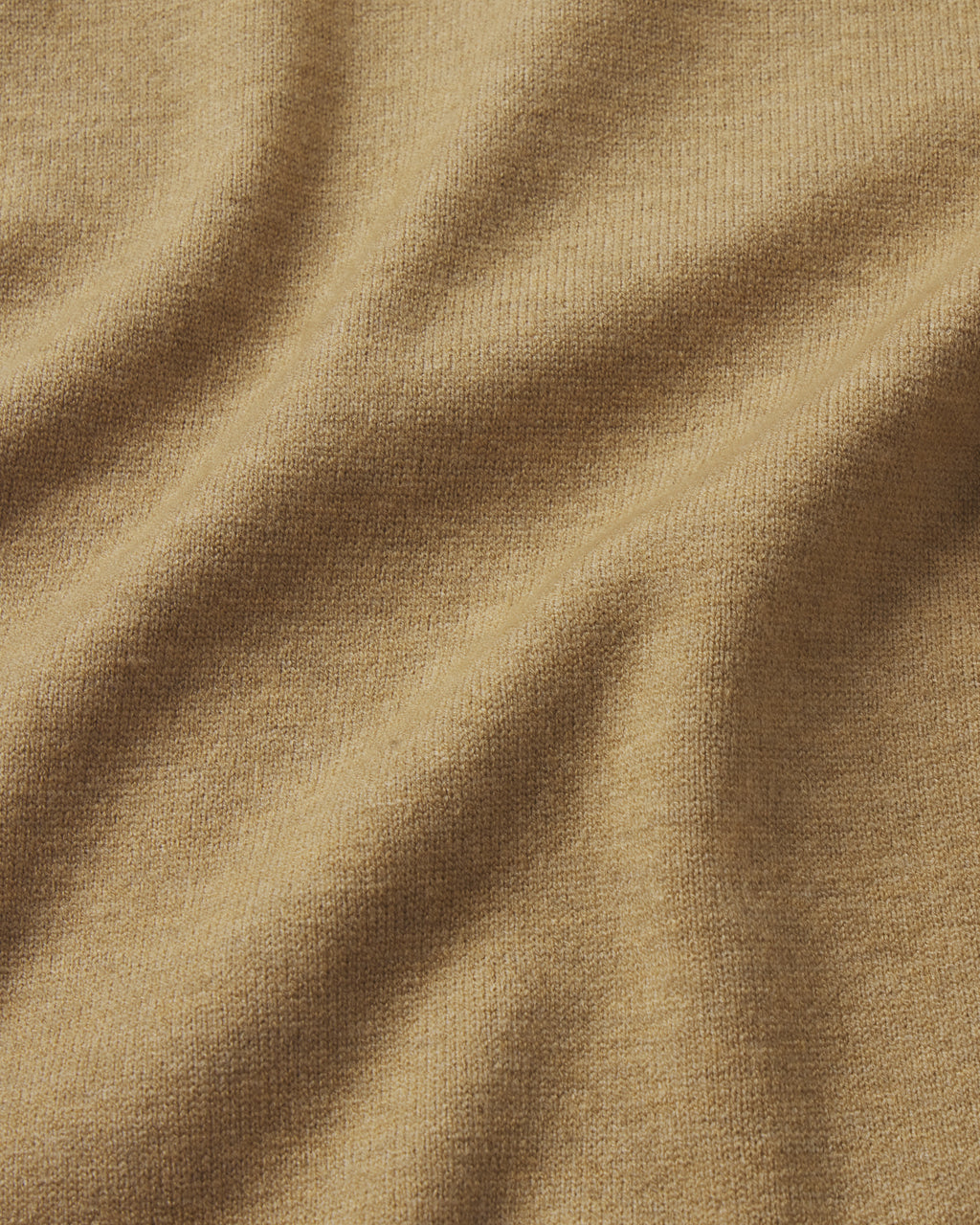 A close-up of the Vesper Crew Neck Set in Sandstone Heather shows softly folded, light beige fabric with a smooth, fine texture and slight stretch—capturing the cozy feel ideal for jogger-style comfort.