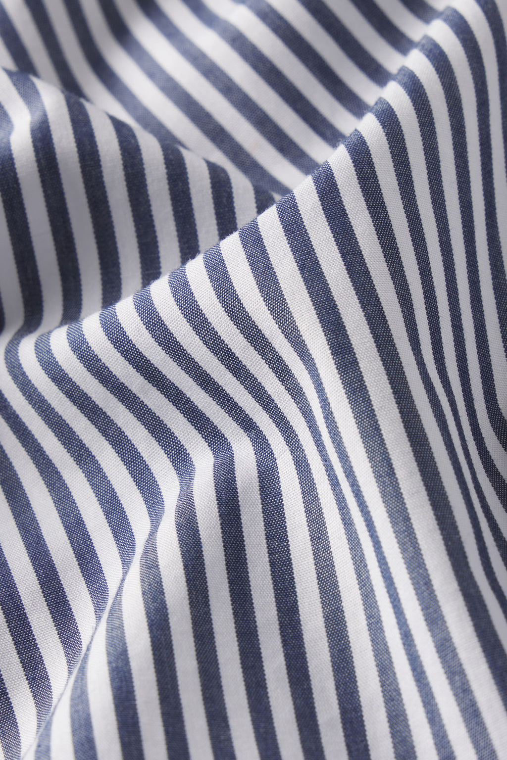 A close-up of the Poplin Piped Long-Long Set in English Navy Riviera Stripe shows white cotton sleepwear with evenly spaced, vertical navy blue stripes and gentle, fabric curves from slight wrinkling.