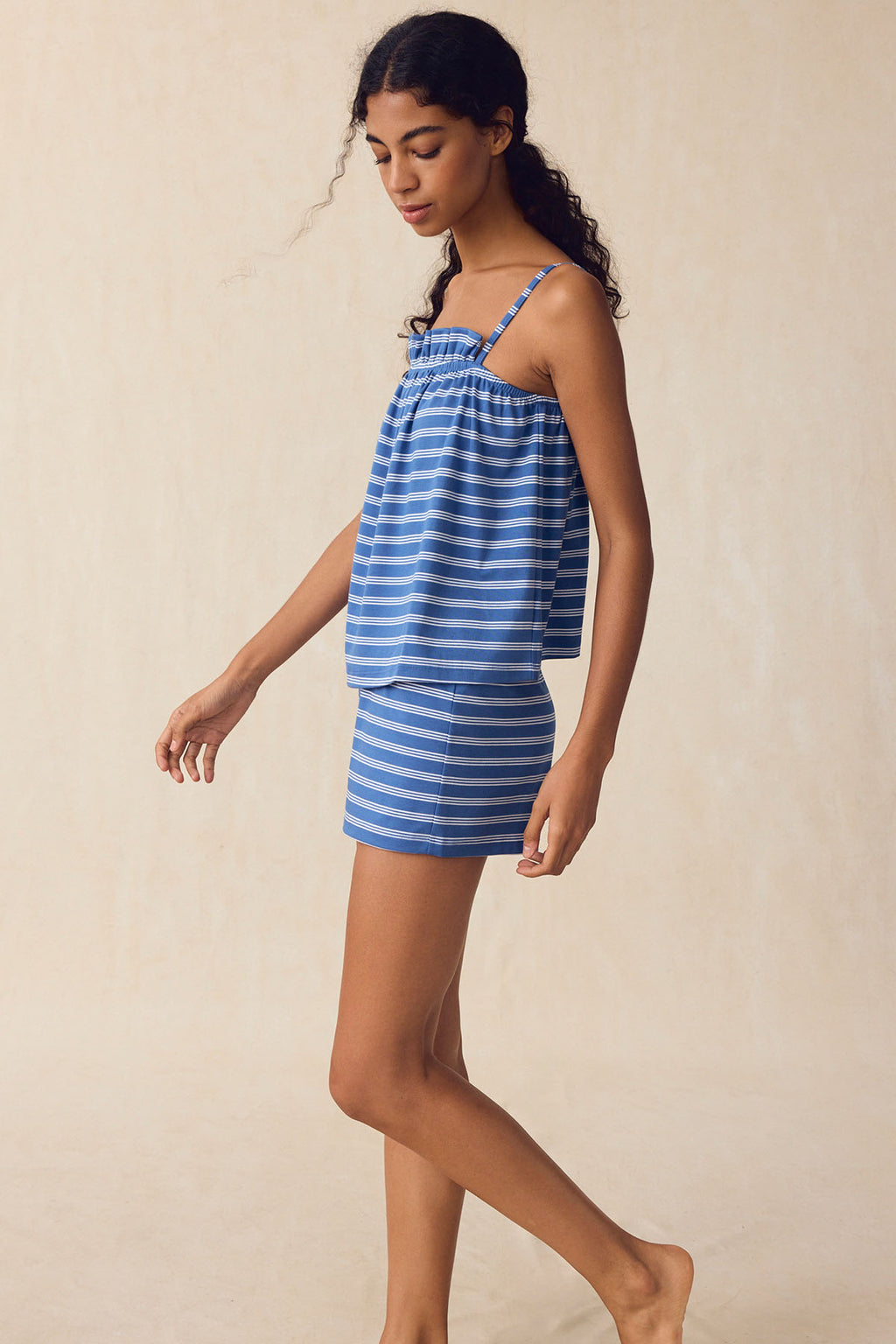 A woman models the Pima Ruffle Shorts Set in Seaport Triple Stripe—featuring a sleeveless top and matching shorts—in front of a light beige background.