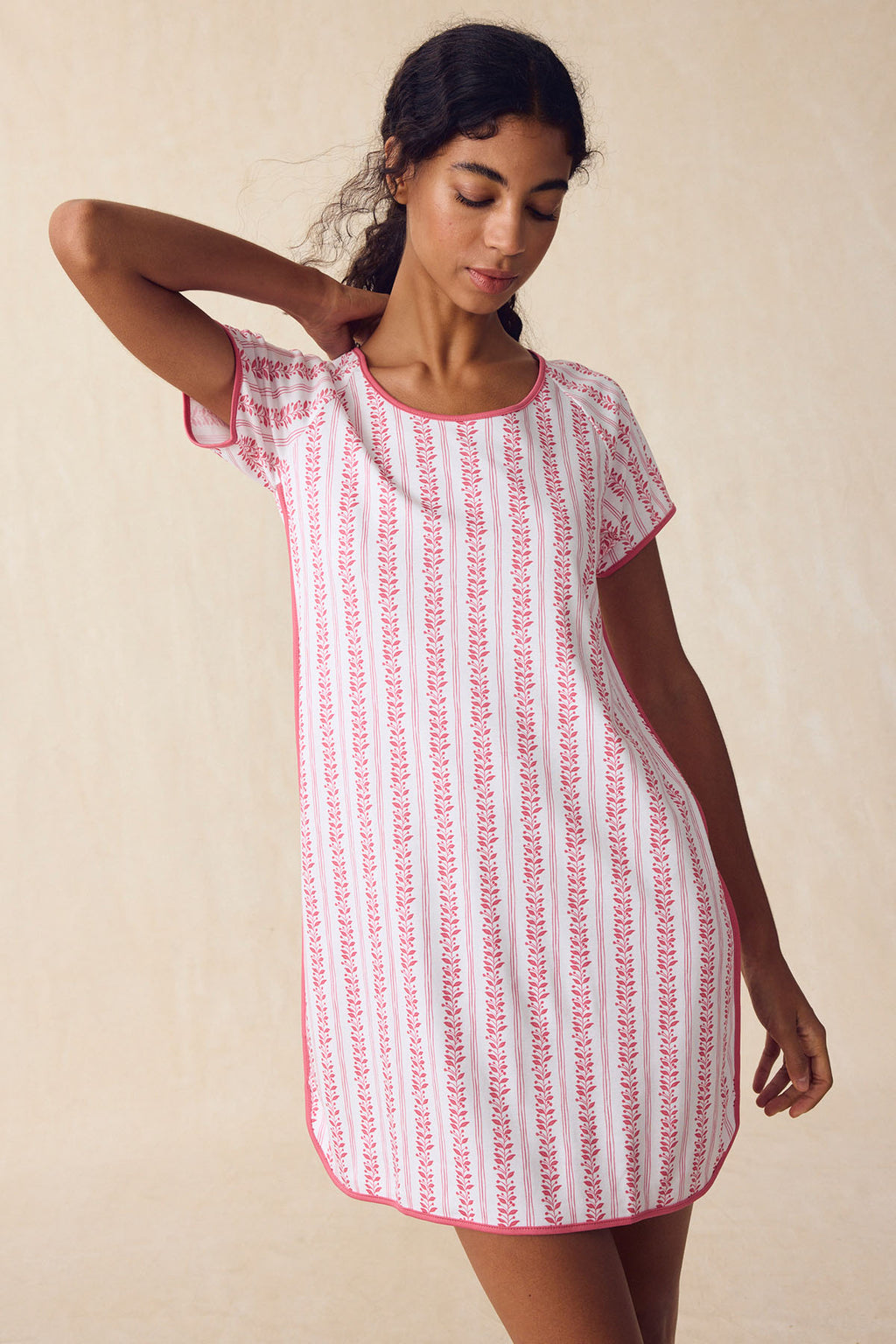 A woman models the Pima Nightgown in Winterberry Jasmine Vine, a short-sleeved, knee-length dress with pink stripes and floral patterns, posing with one hand behind her head against a neutral background.