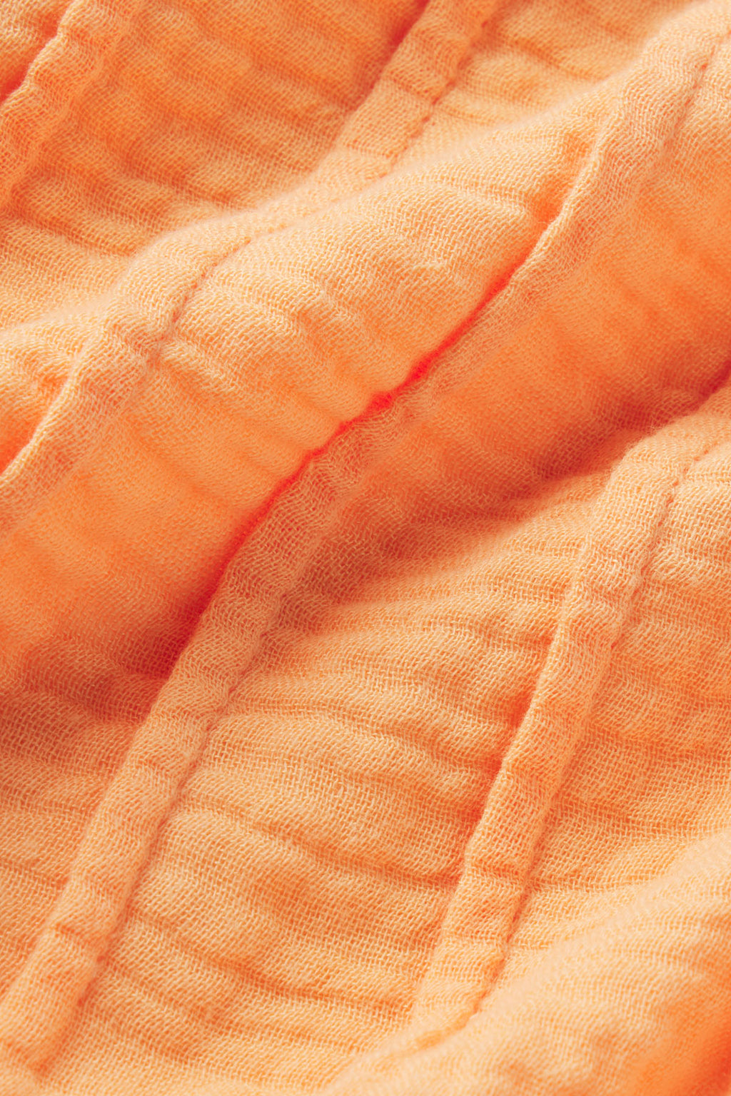 Close-up of the Monaco Shorts Set in Marigold Gauze, featuring textured orange cotton fabric with visible stitching and soft, crinkled folds.