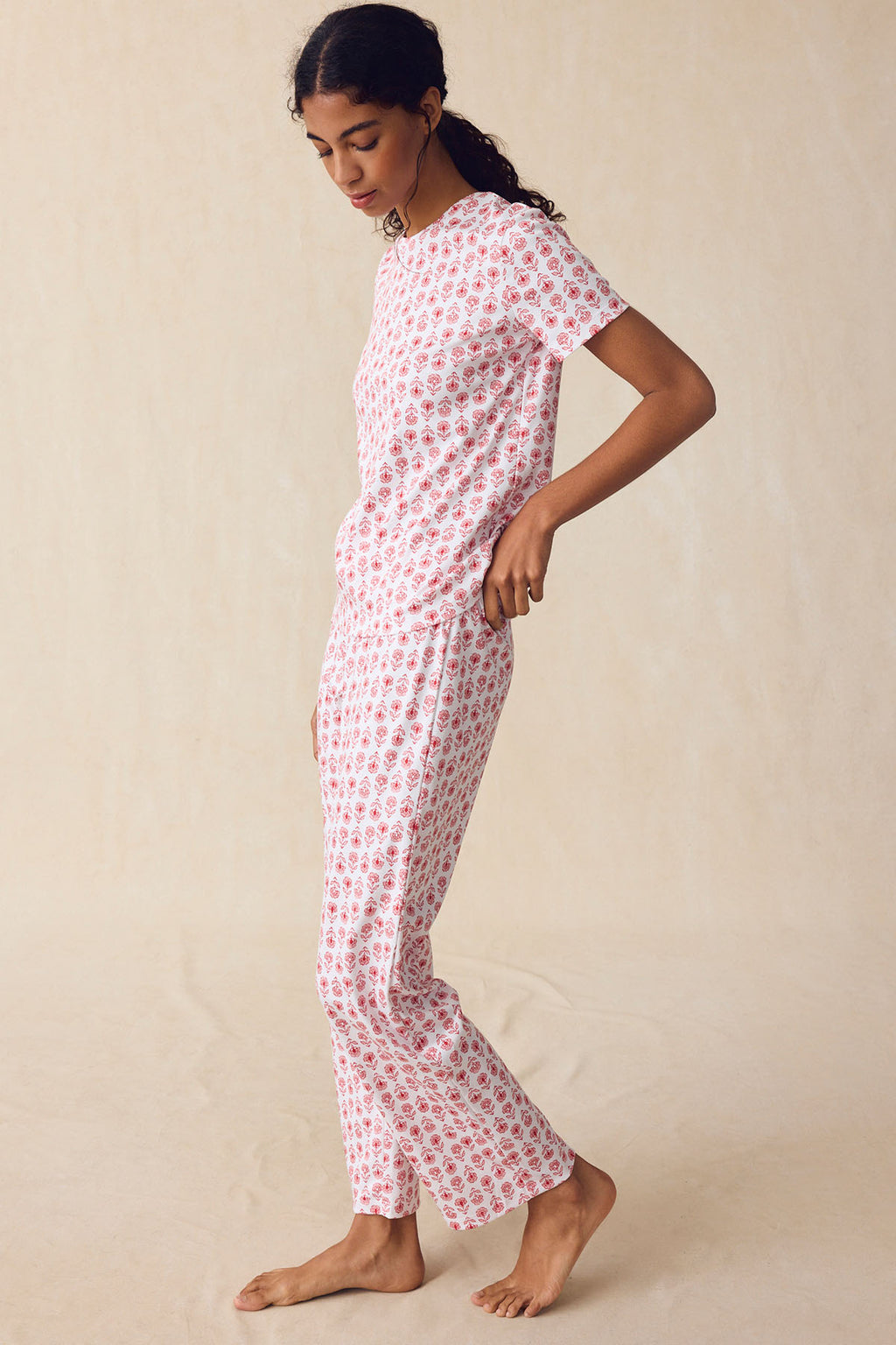 A person stands in profile against a plain background, wearing the Pima Crew Short-Long Set in Rosewater Sprig—a matching short-sleeve shirt and high-waisted pants with a small floral block print on white Pima cotton.