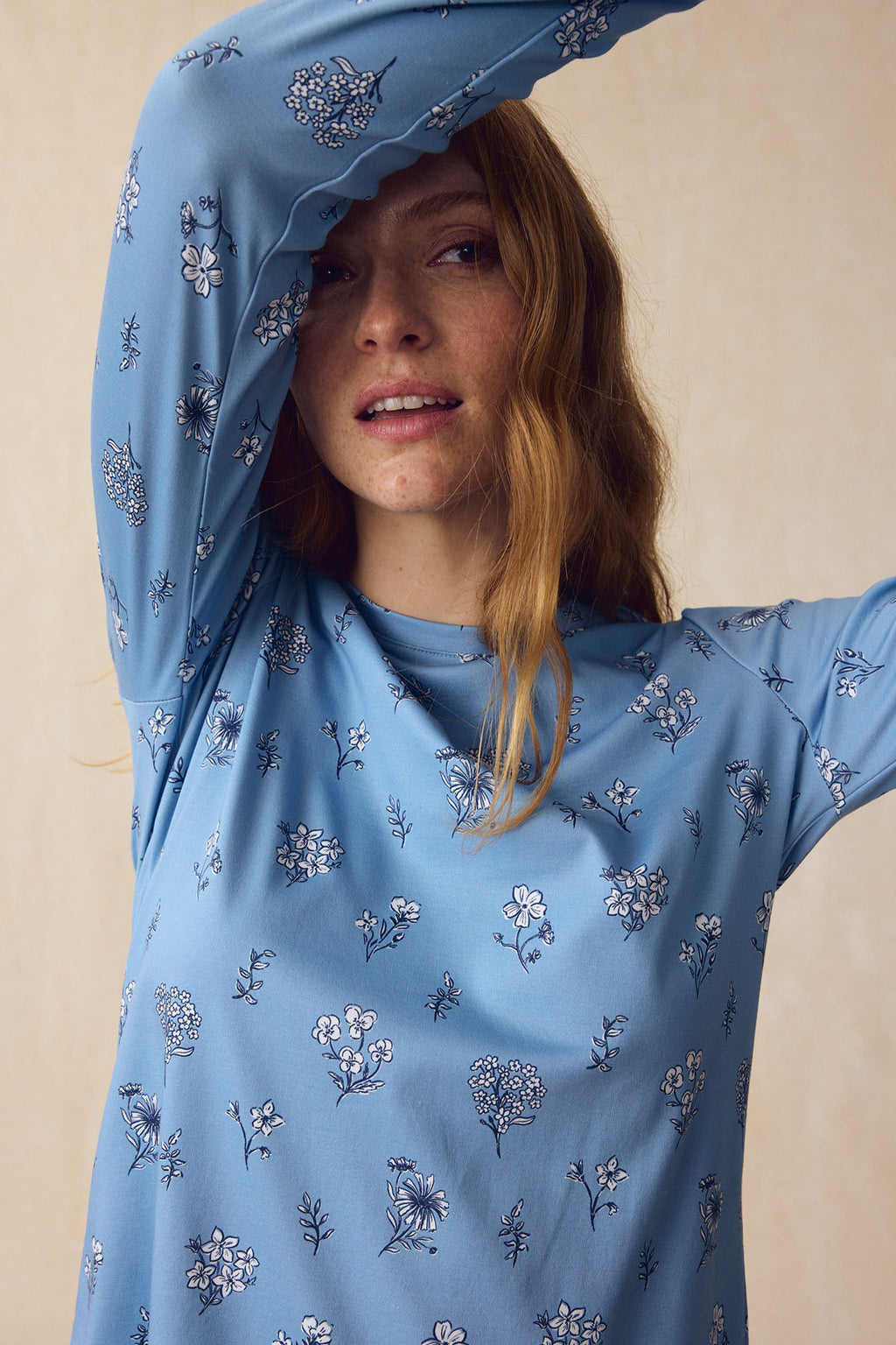 A woman wears the Pima Crew Long-Short Set in Serene Blue Adeline Floral, made from soft Pima cotton, raising one arm and looking at the camera with a neutral expression.