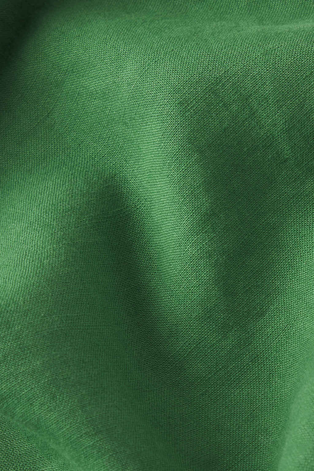 A close-up of the Flute Skirt Set in Palm shows emerald green linen with visible texture and subtle folds, casting gentle shadows and highlights that suggest a tailored fit.