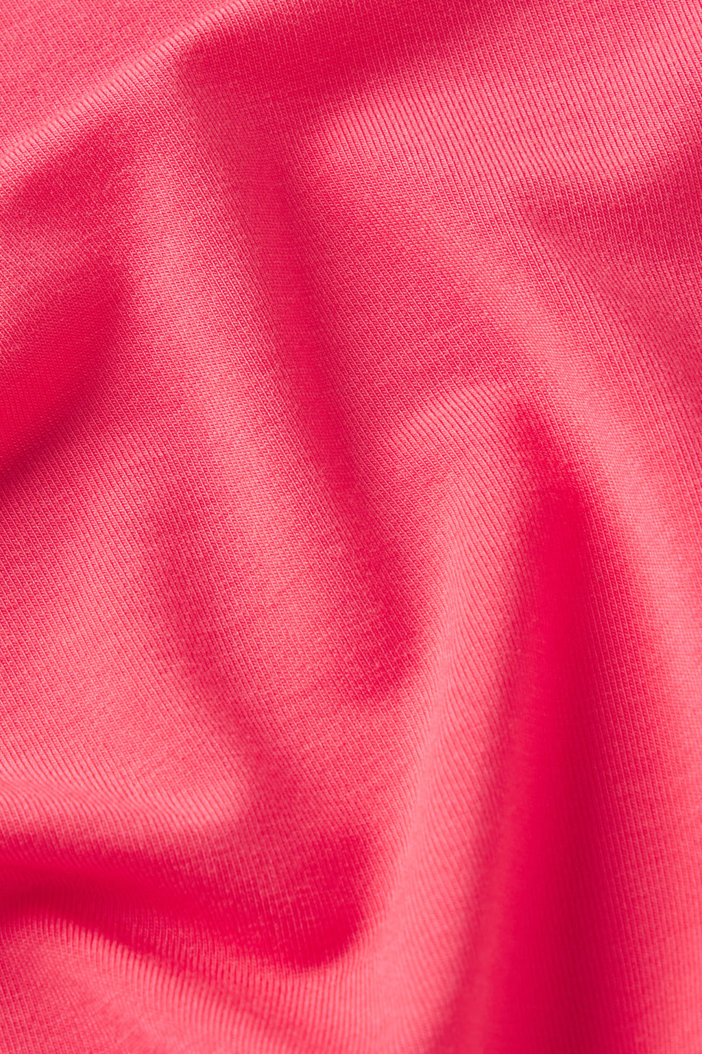Bright pink ribbed fabric with draped folds showing texture and depth.
