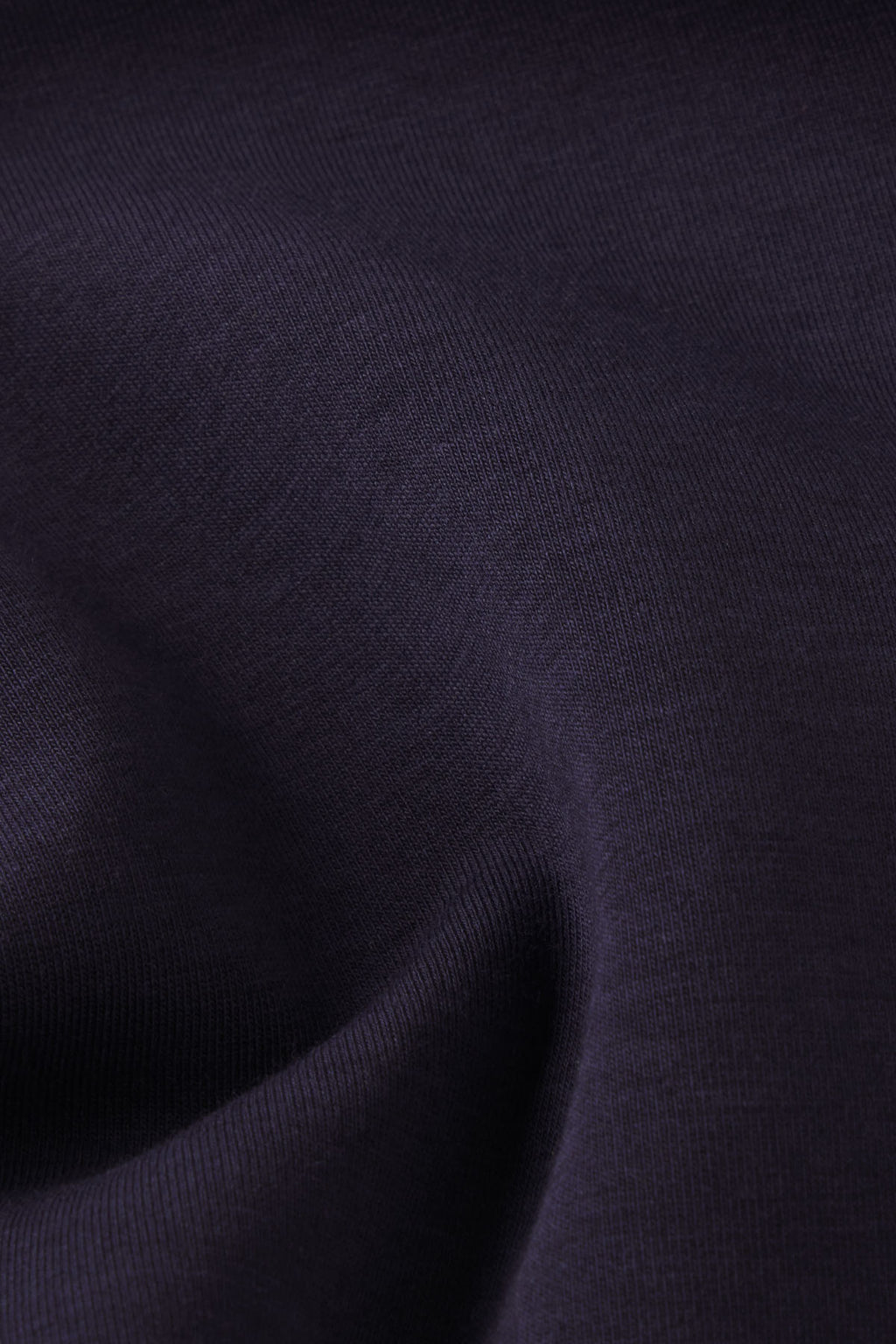 Close-up of the Dash Dress in Maritime, featuring dark, smooth fabric with fine texture and flowing folds that create soft shadows and highlights, evoking the elegance of a stretch knit dress.