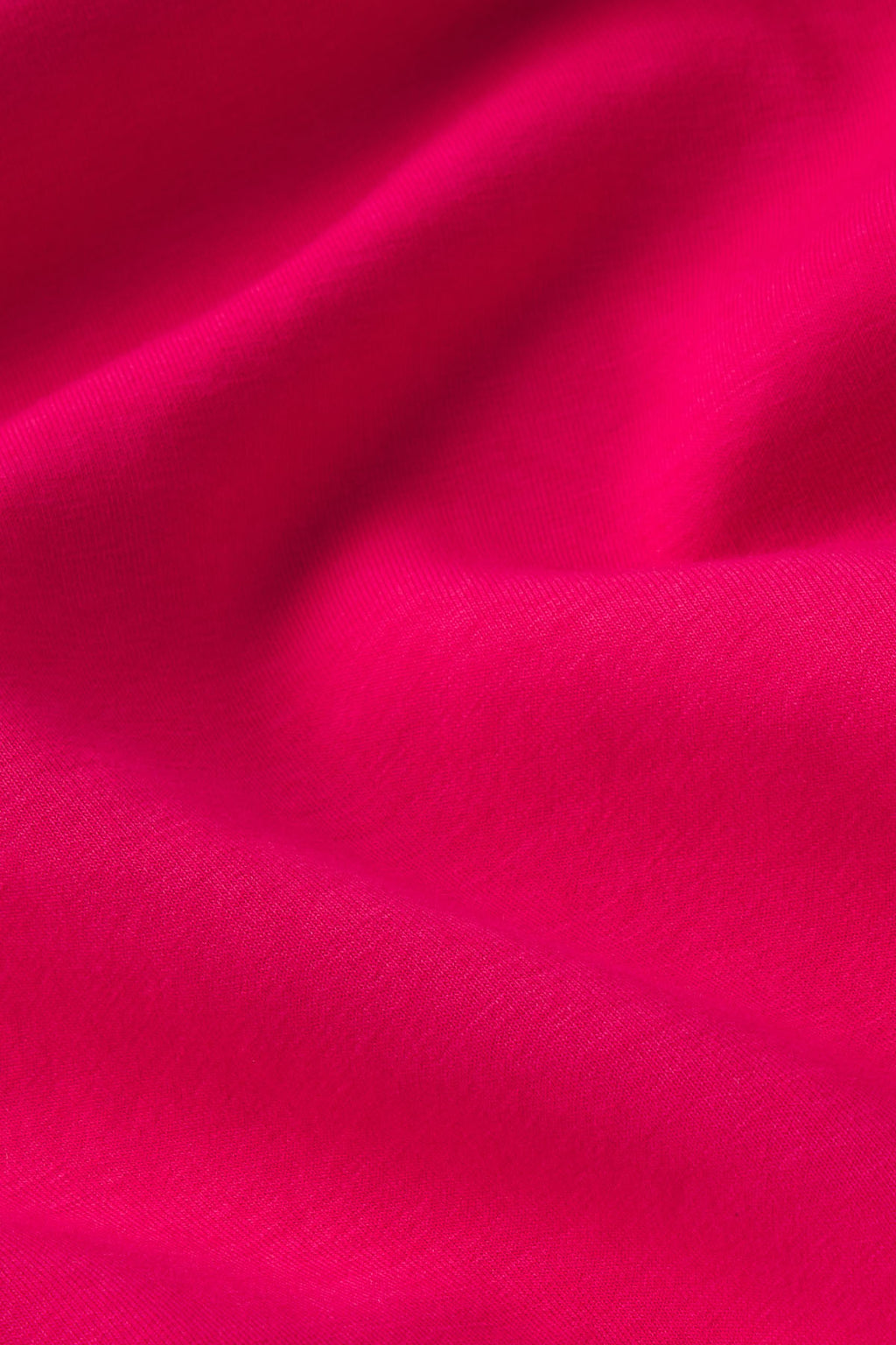 Close-up of the Dash Dress in Magenta shows bright pink fabric with visible texture, gentle folds, and soft shadows and highlights across the material.