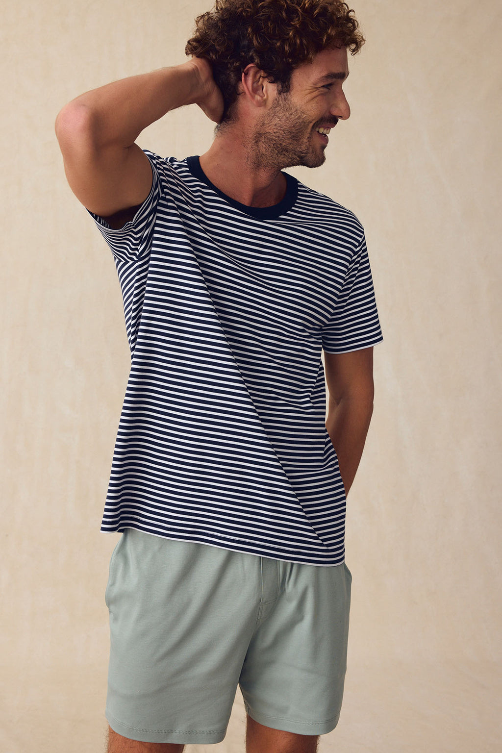 A man smiles with one hand behind his head, wearing the Men