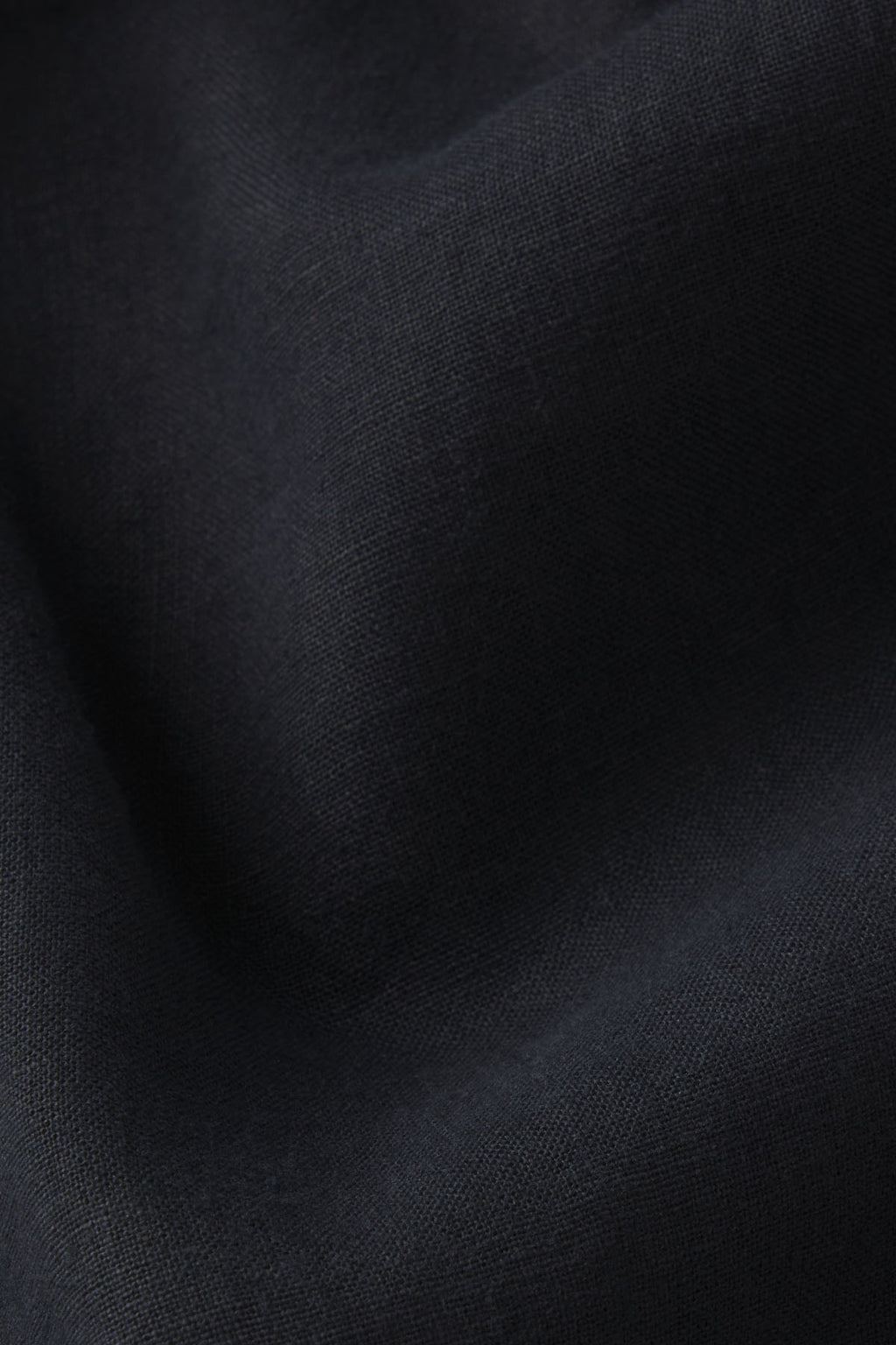 Close-up of the Coupe Pant Set in Black, showing its textured linen fabric with gentle folds that create soft shadows and highlights on the surface.