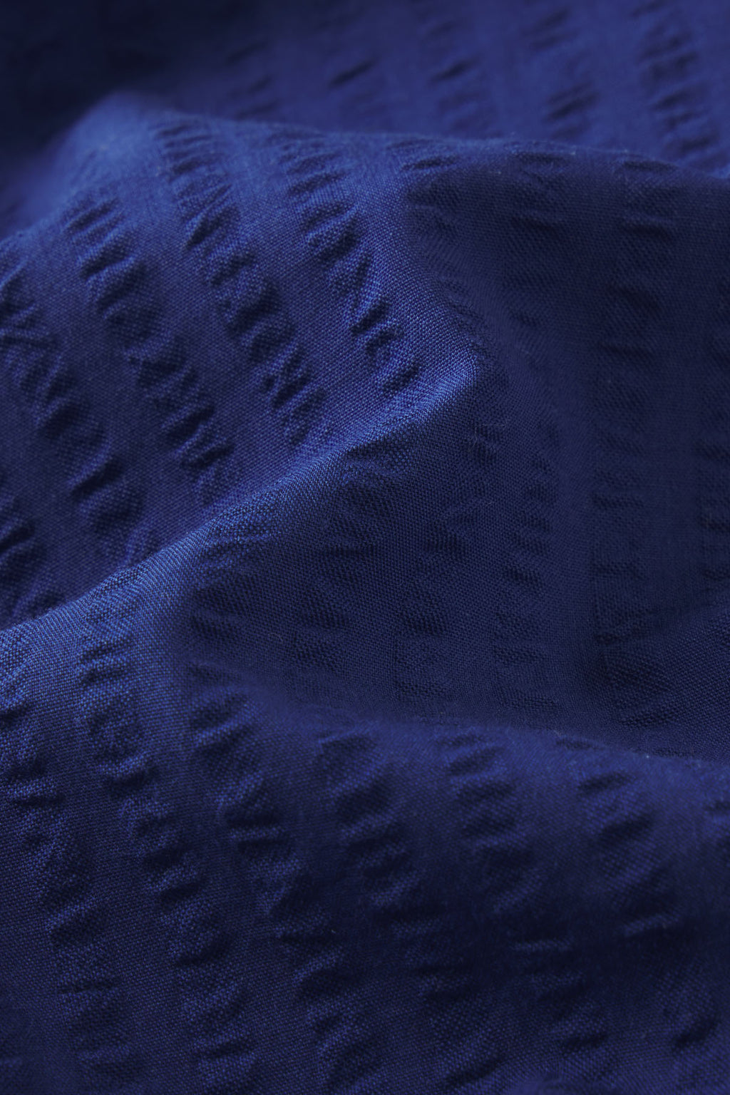 Close-up of the Charlie Shorts Set in Blue Depths Seersucker, showcasing Pima cotton fabric with subtle horizontal ridges, woven patterns, gentle folds, and soft shadows.