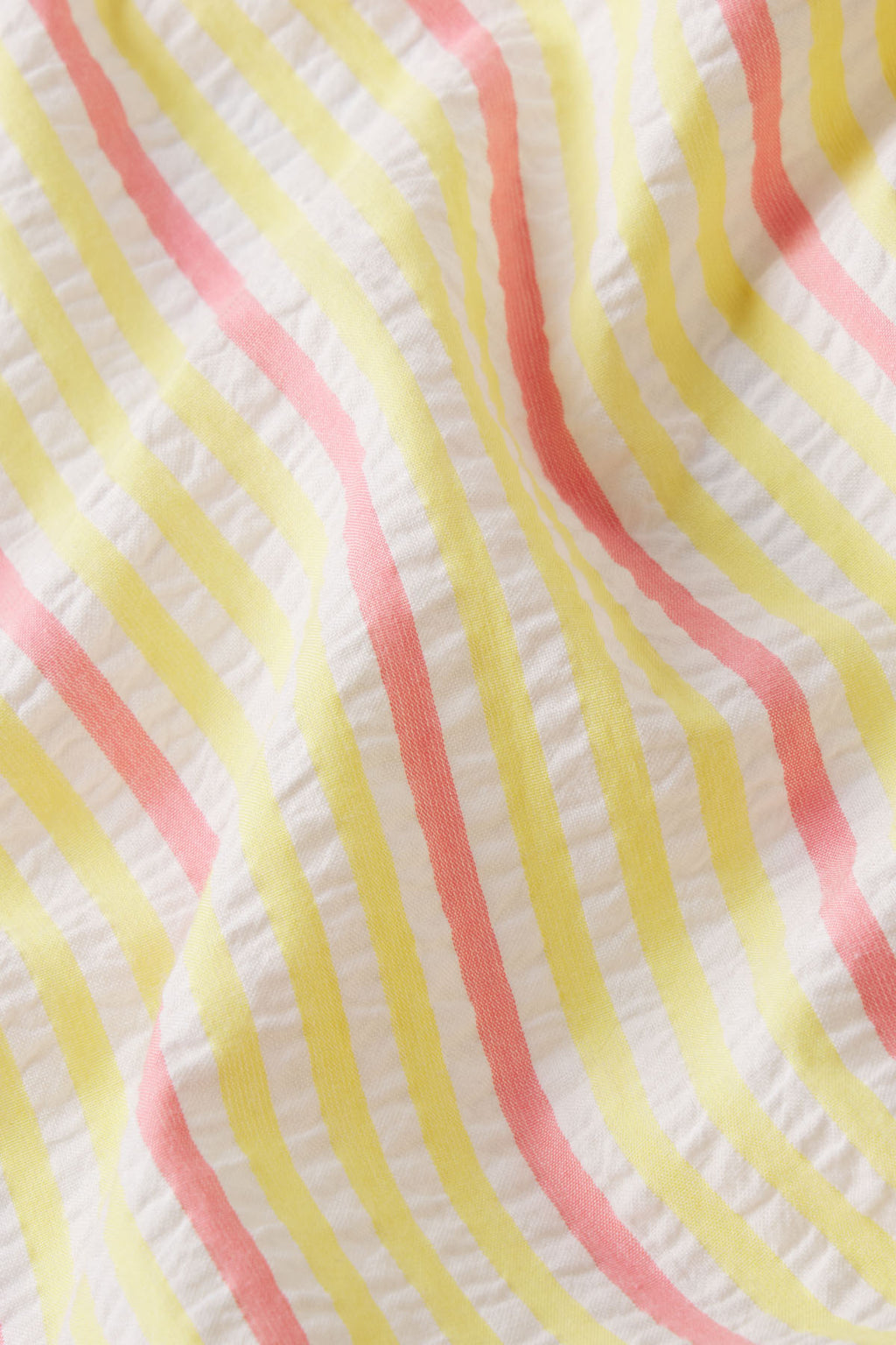 A close-up of the Alice Nightgown in Zest Coastline Seersucker, showing its crinkled fabric with vertical pastel yellow and pink stripes on a white background.
