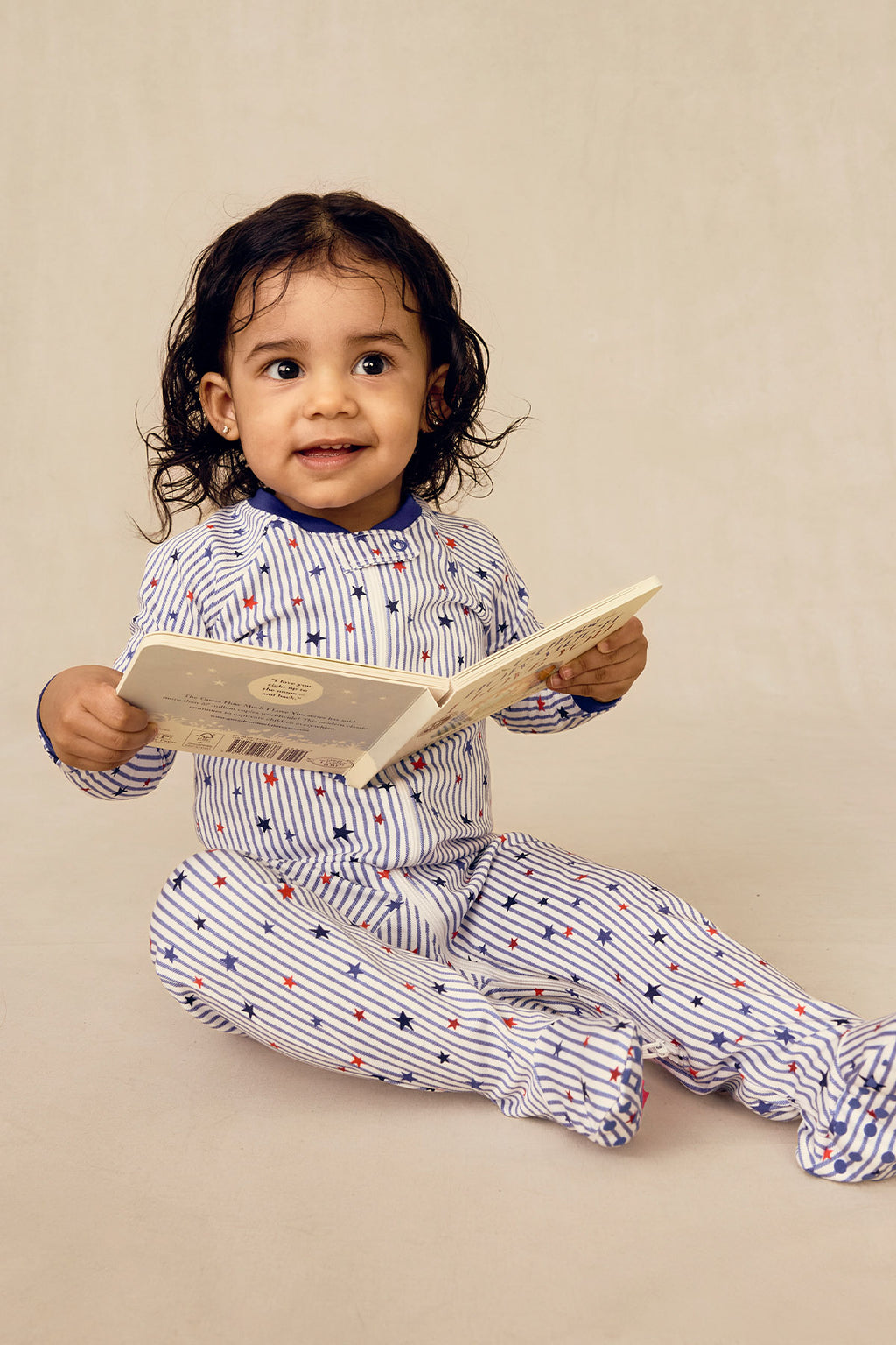 Toddler wearing white sleeper with blue stripes and red and blue stars throughout.