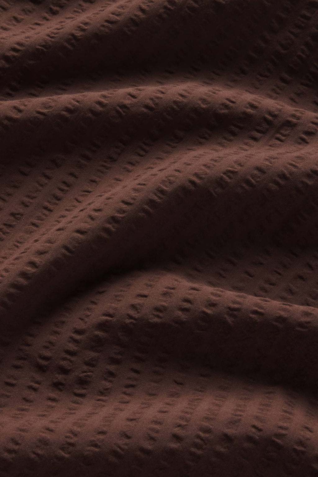 Cocoa brown seersucker fabric with textured striped pattern and folded layers.