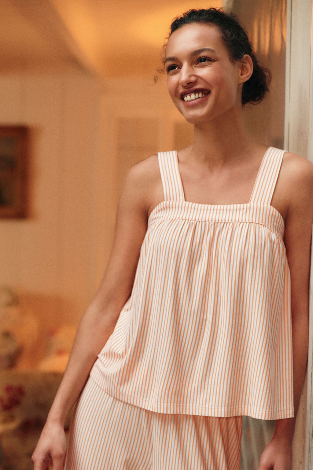 Woman wearing marigold and white vertical striped sleeveless top and matching pants.
