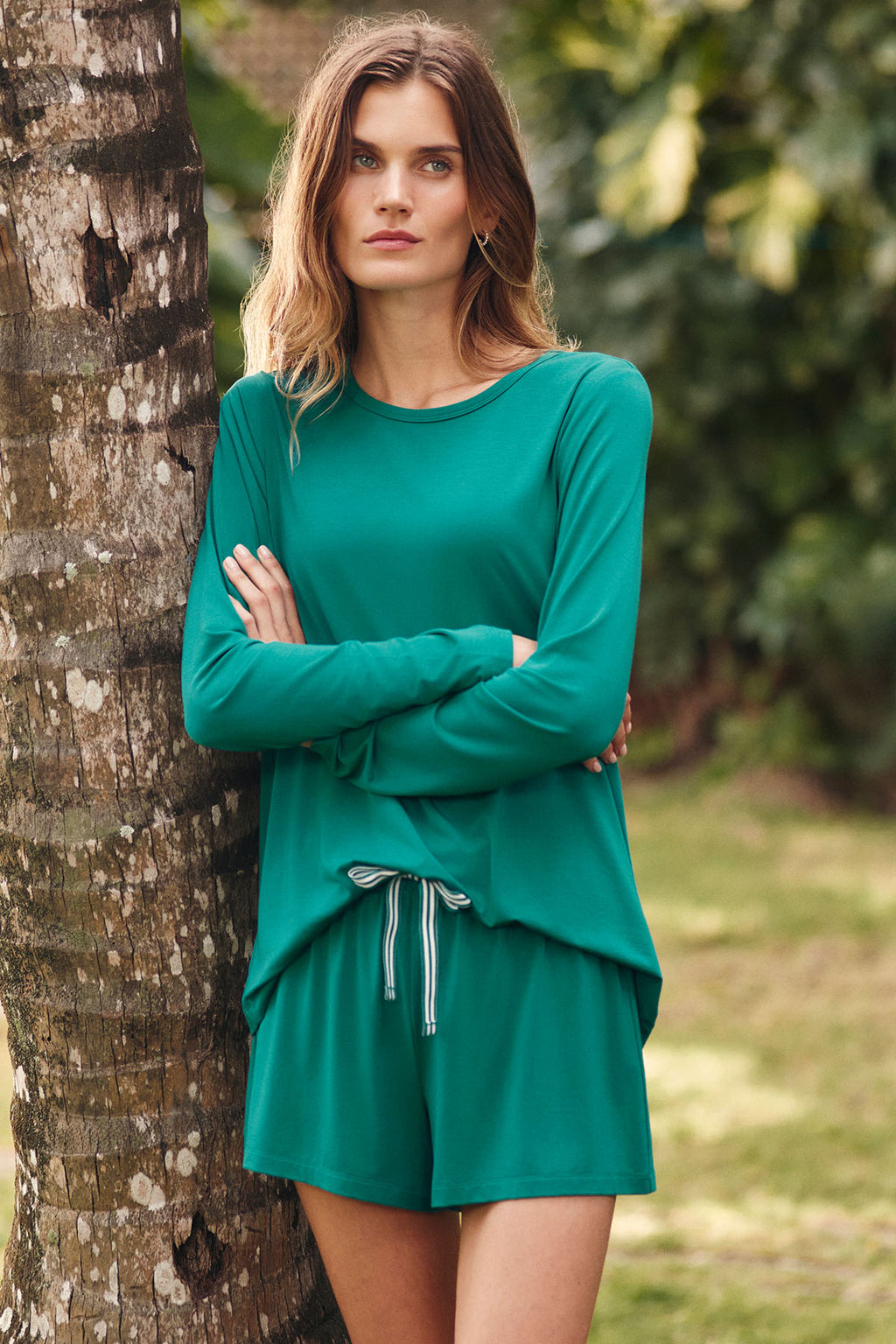 Woman wearing teal long-sleeve dress with ribbon drawstring detail at waist, standing against tree.