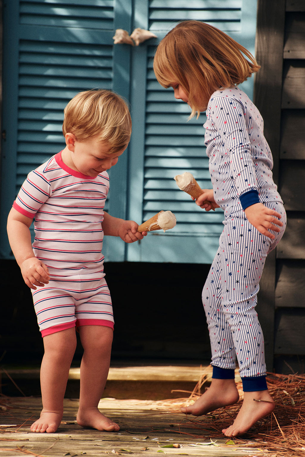Two children wearing striped and star-patterned long pajama sets in red/pink and blue colorways.