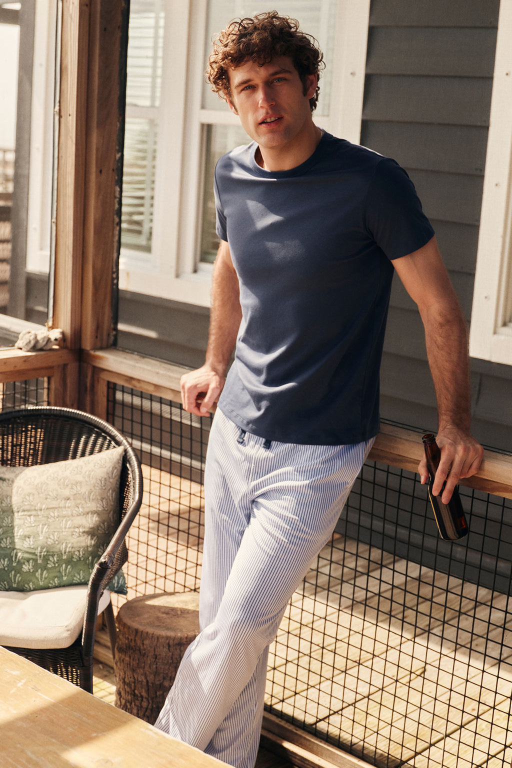 Man wearing navy short-sleeve shirt and white striped long sleep pants standing on a porch.